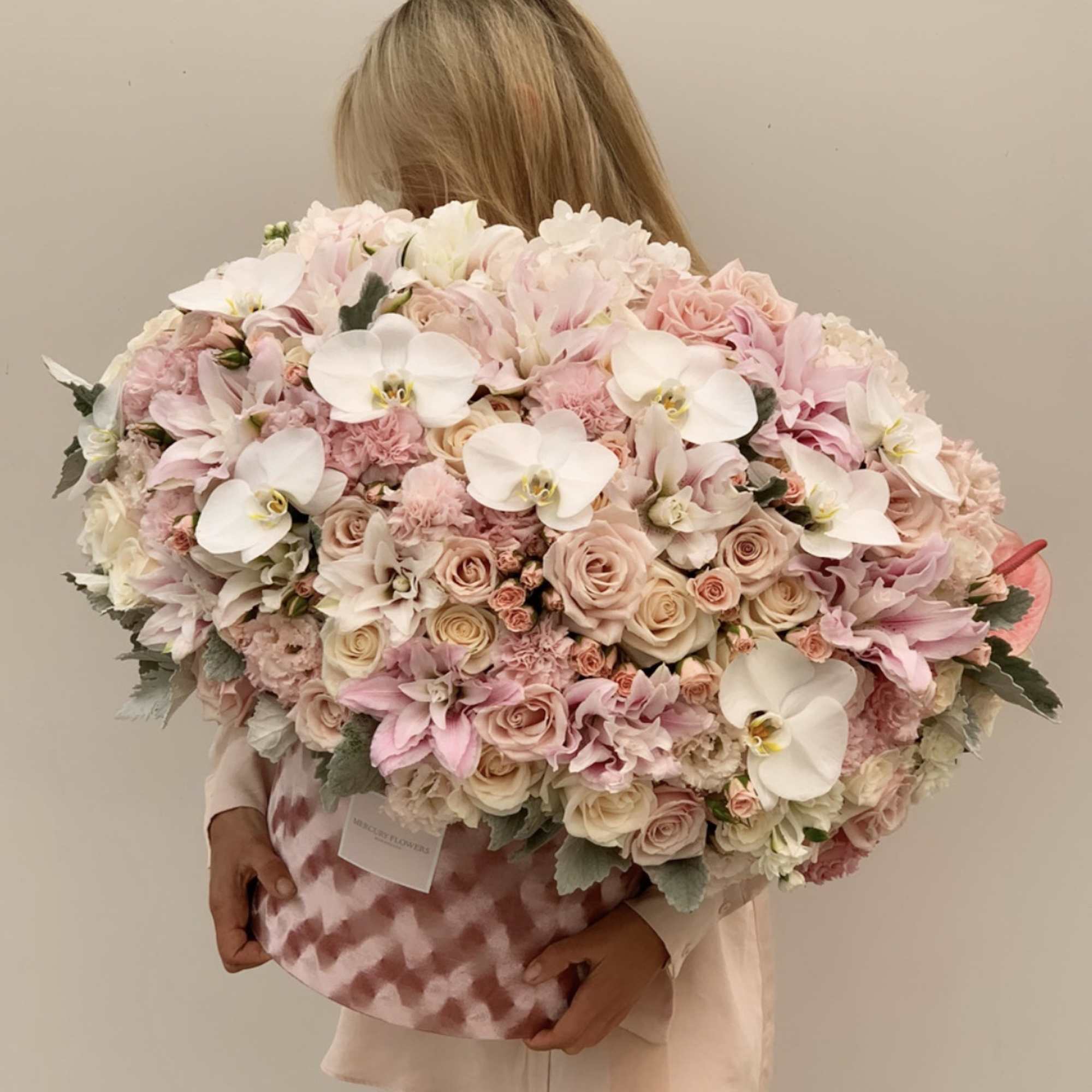 Large pastel bouquet of roses, orchids, and white blooms in a pink patterned box
