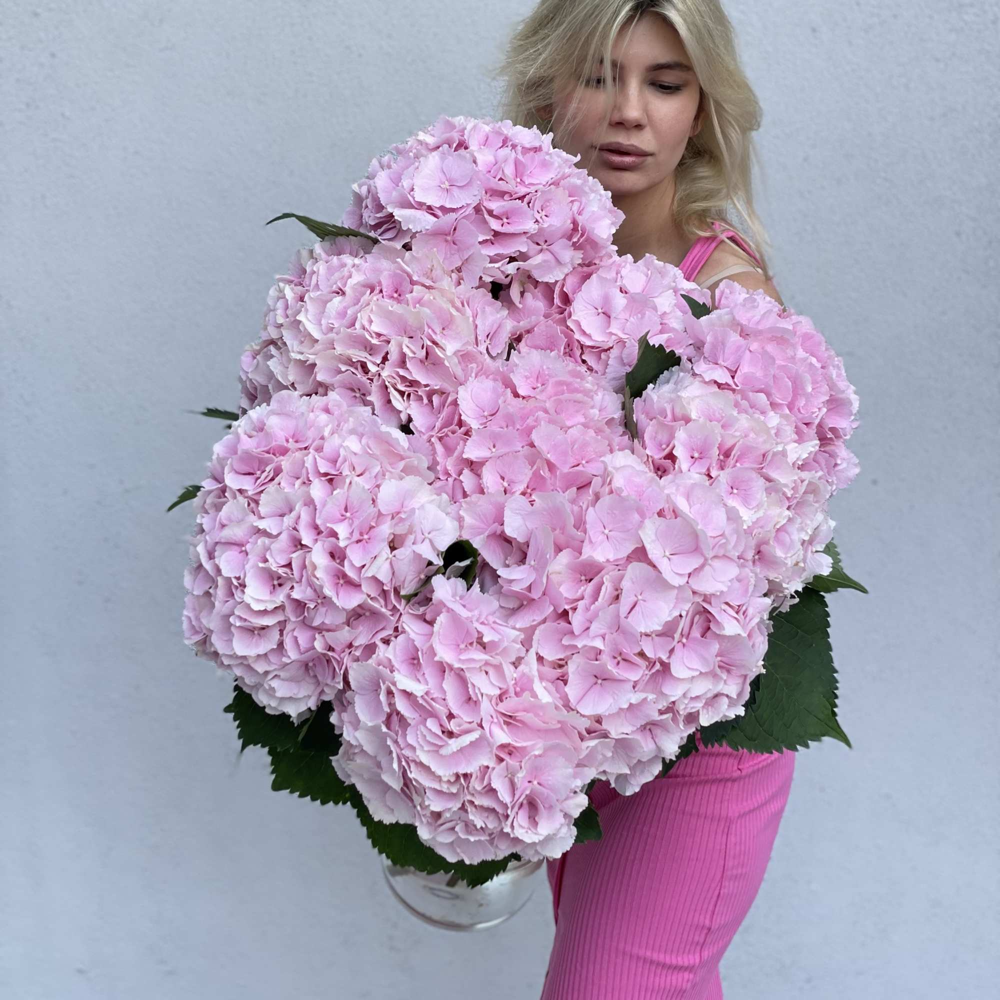 Woman holding a large bouquet of pink hydrangeas in a clear vase