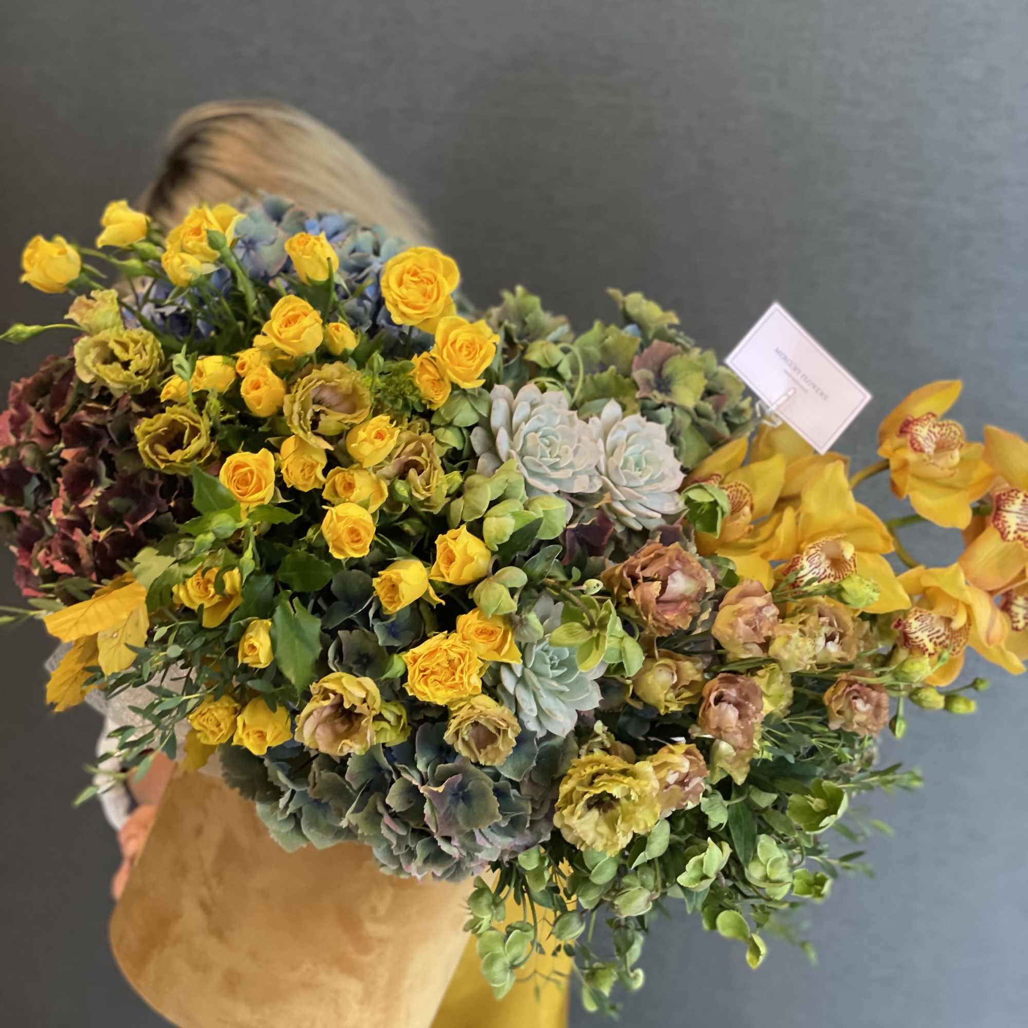 Large bouquet of yellow roses, orchids, and succulents wrapped in tan paper