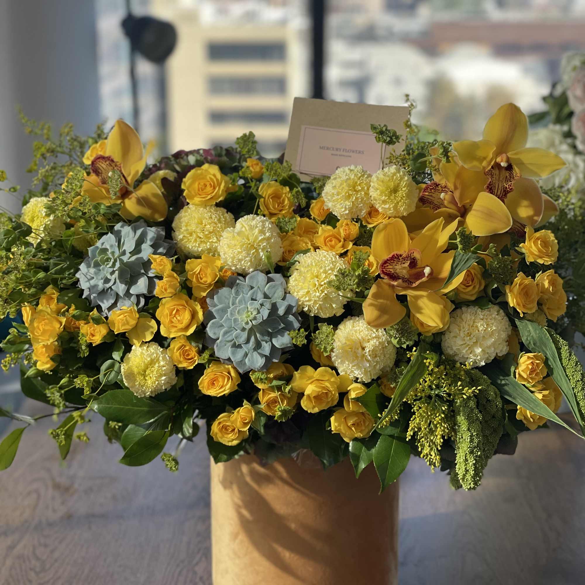 Yellow floral arrangement in a round box with roses and orchids