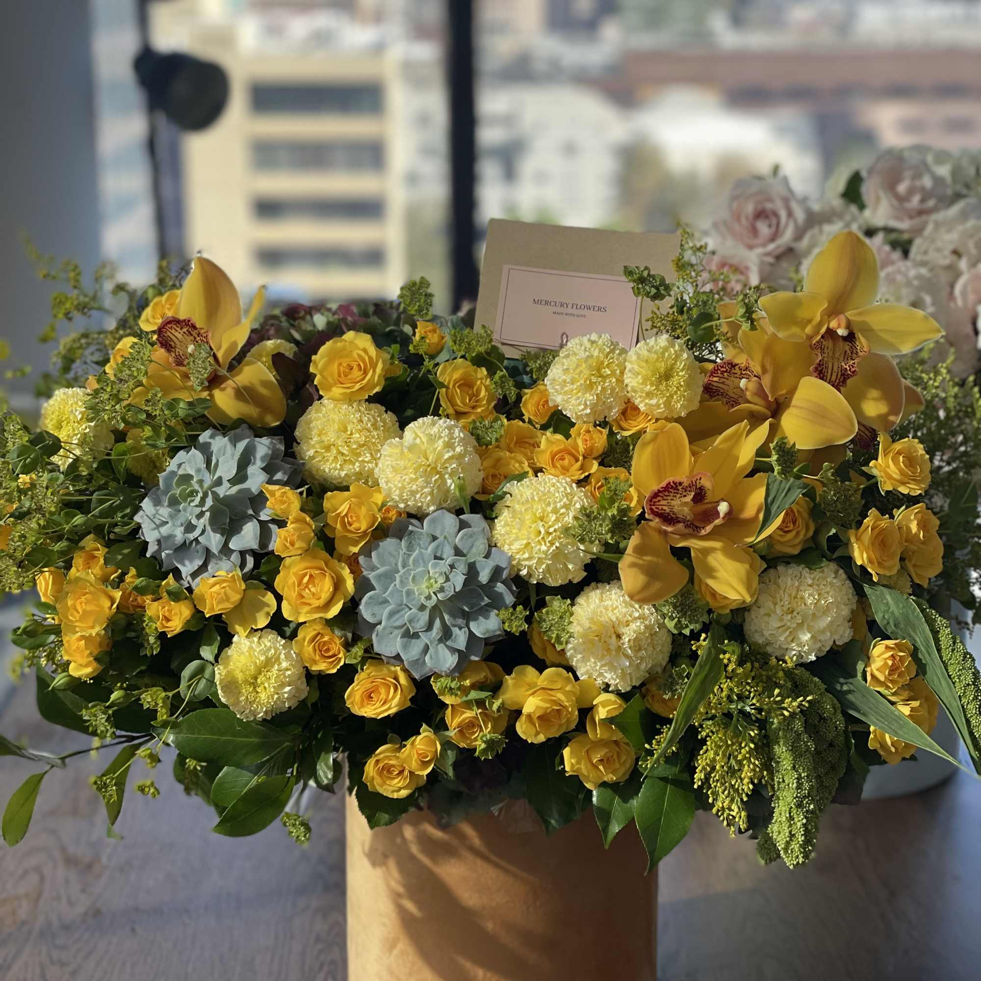 Yellow roses and orchids arranged in a tan hat box
