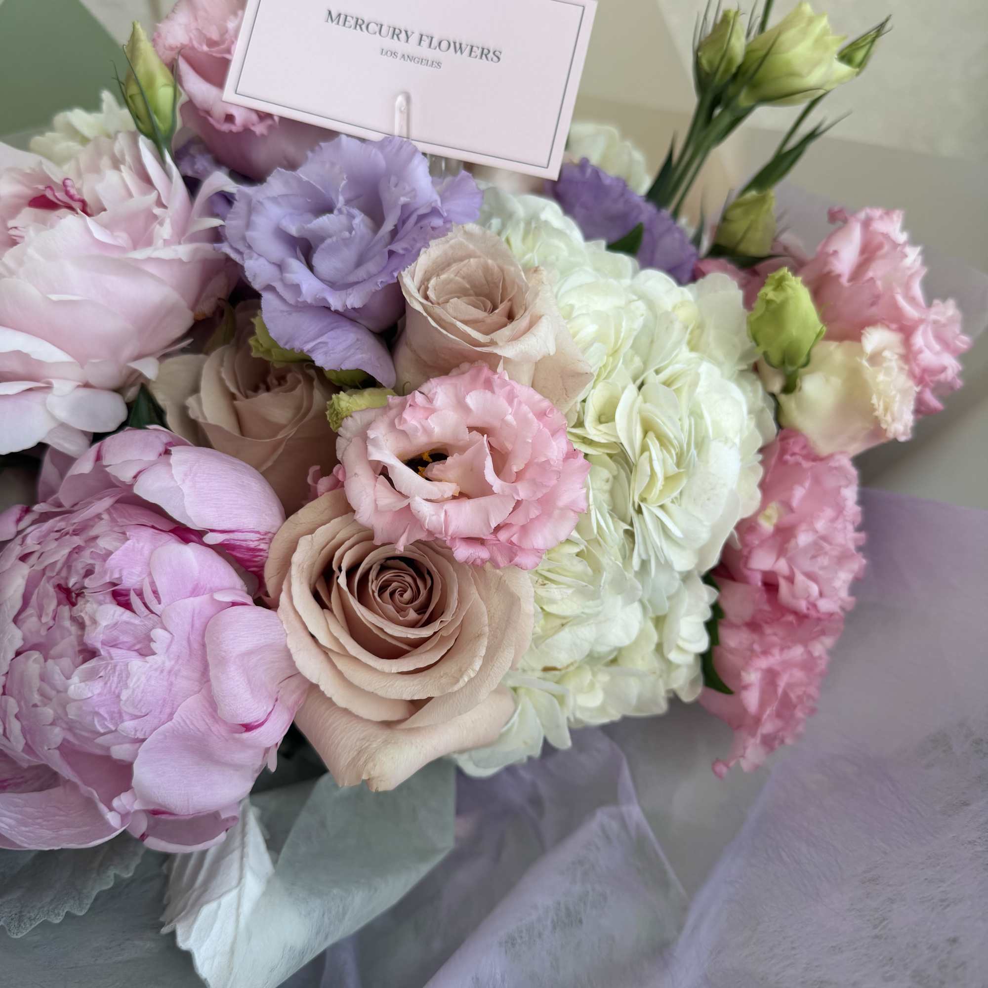 Pastel bouquet of roses, peonies, and lisianthus with a card