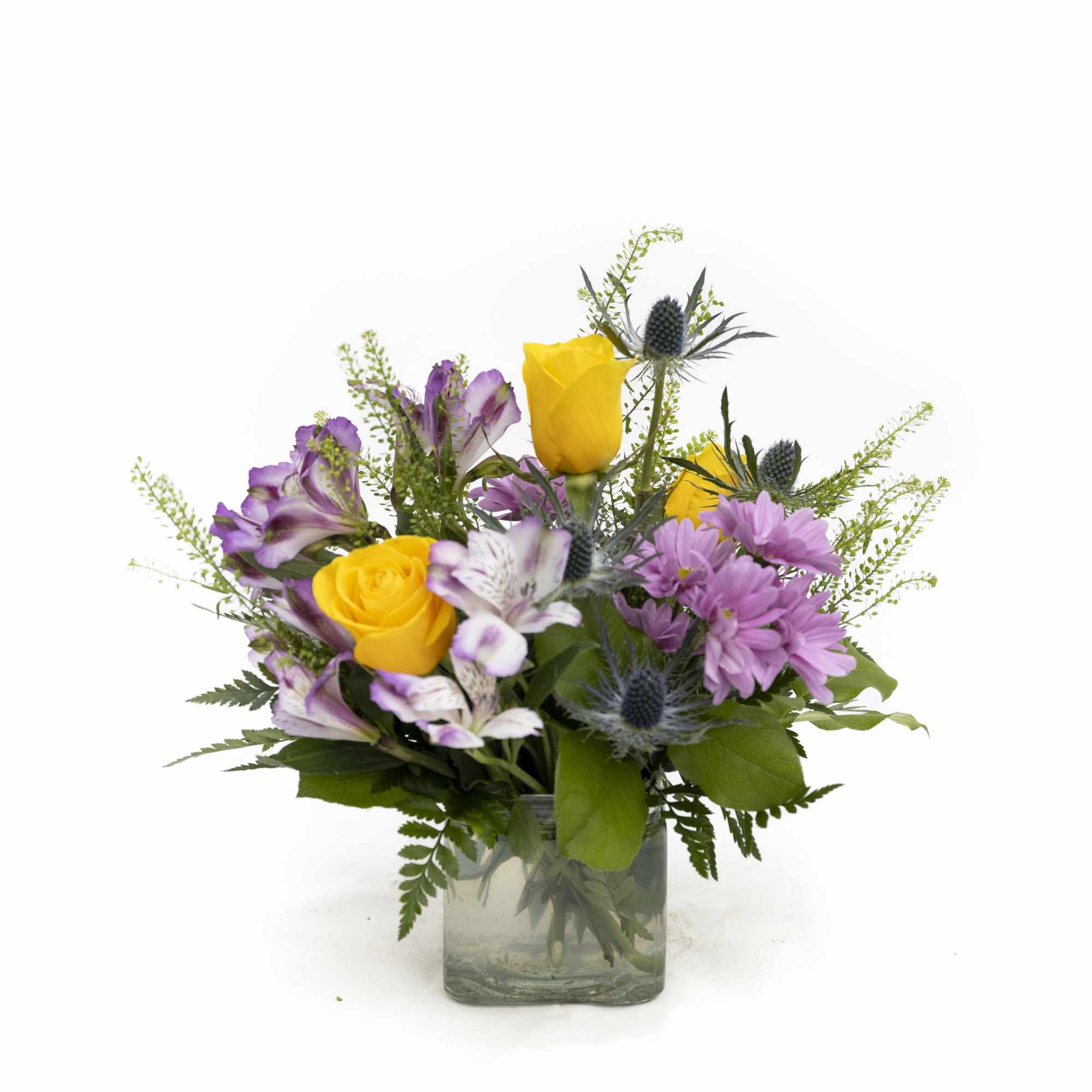 Mixed bouquet of yellow roses and purple flowers in a clear glass cube vase