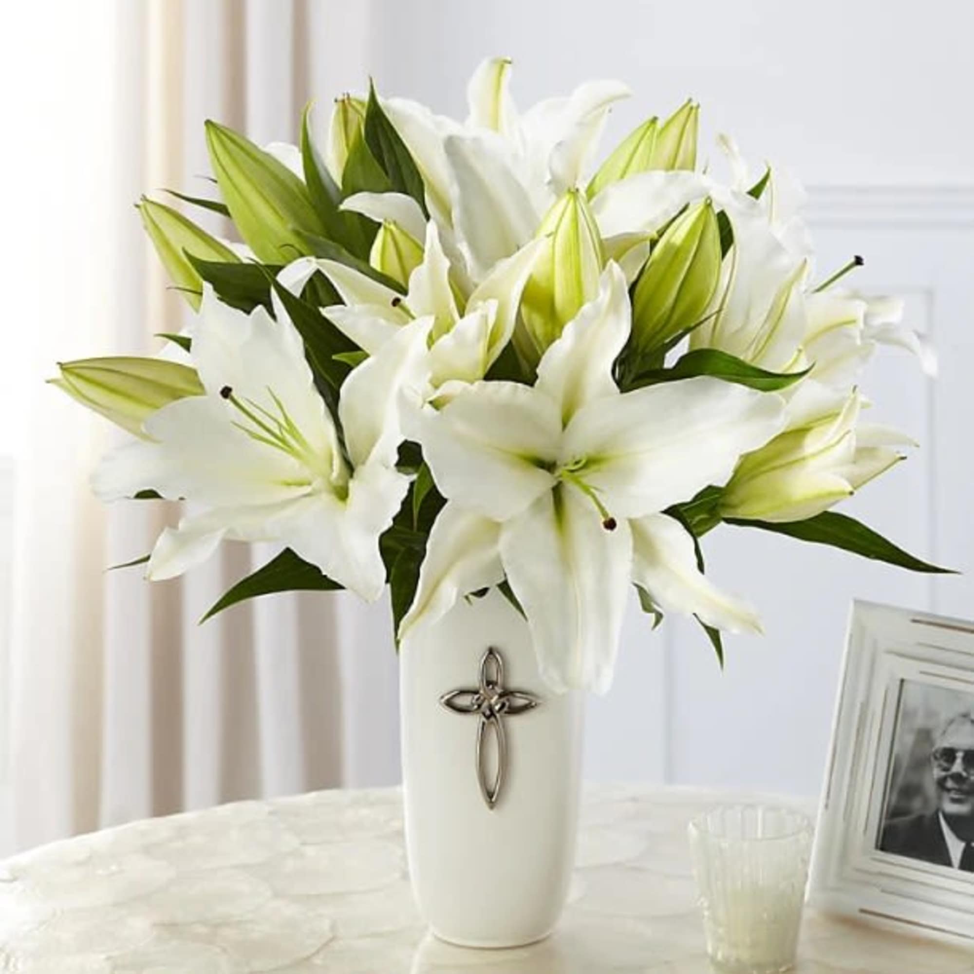 White lilies arranged in a tall white vase with a cross emblem