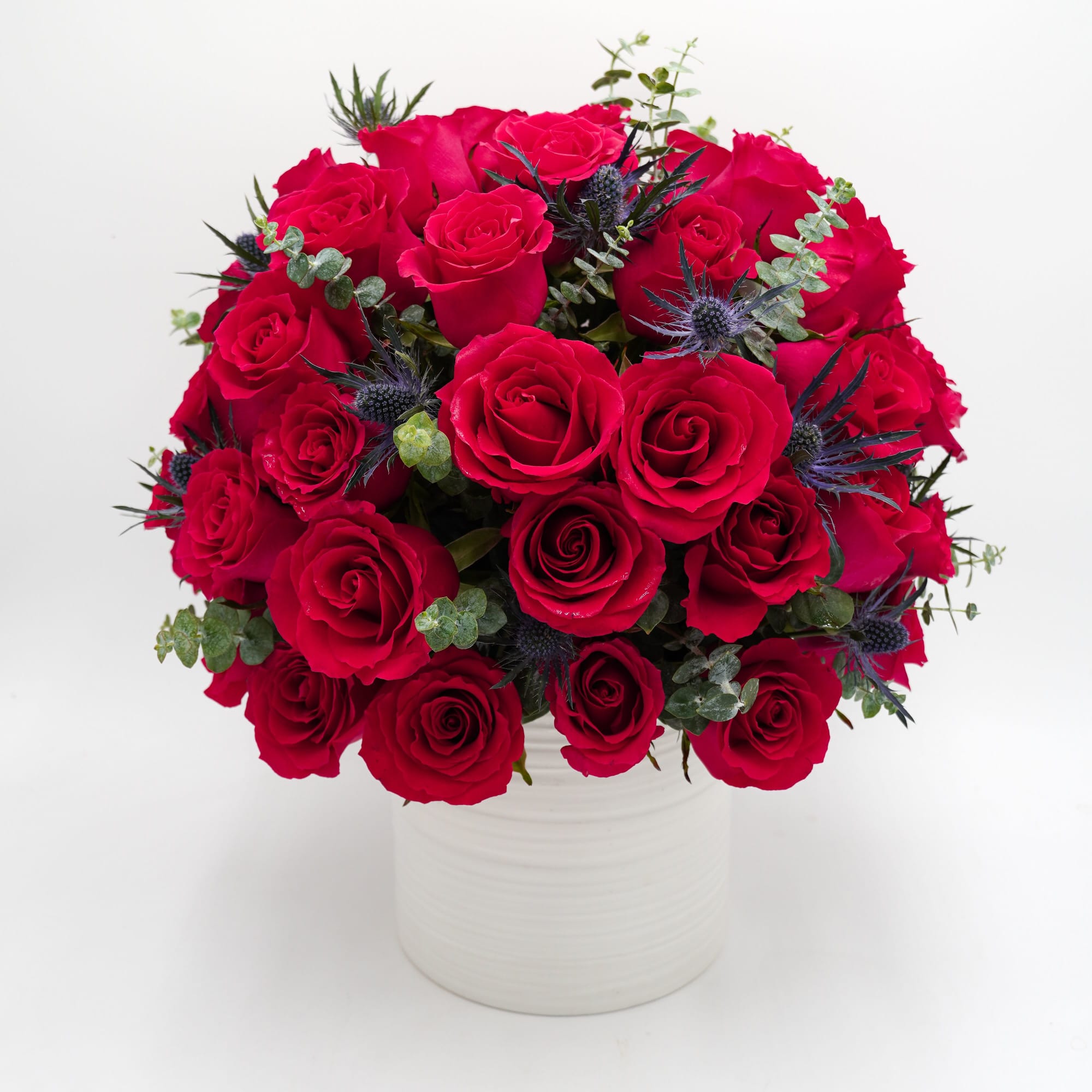 Red rose bouquet in a white vase with blue thistle accents
