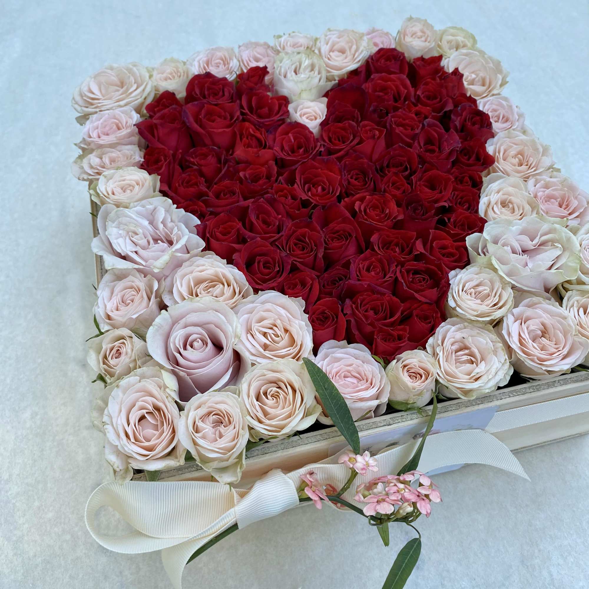 Heart-shaped box of red and pale pink roses with a white ribbon