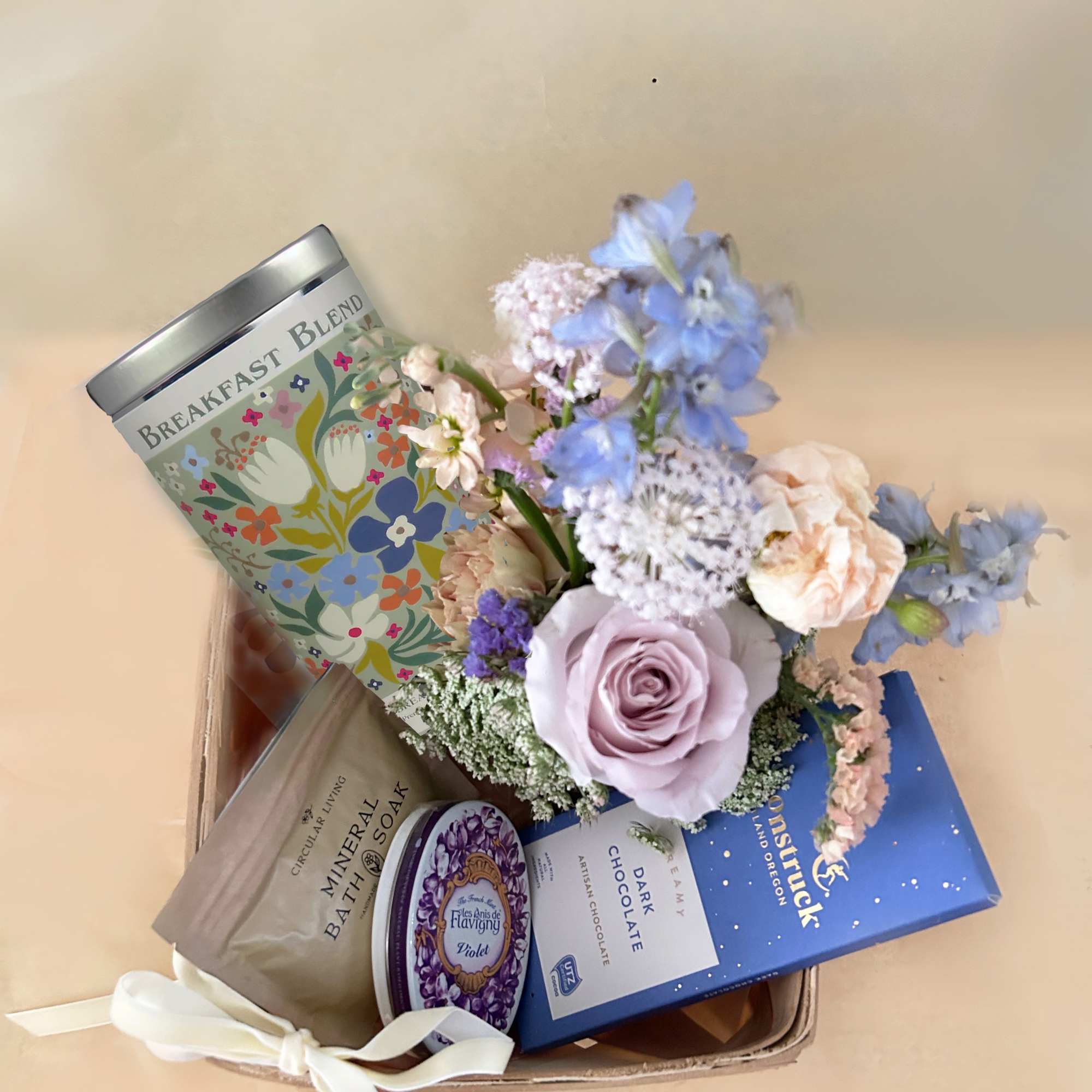 Gift basket with pastel flowers, bath soak, chocolate, and a tea tin