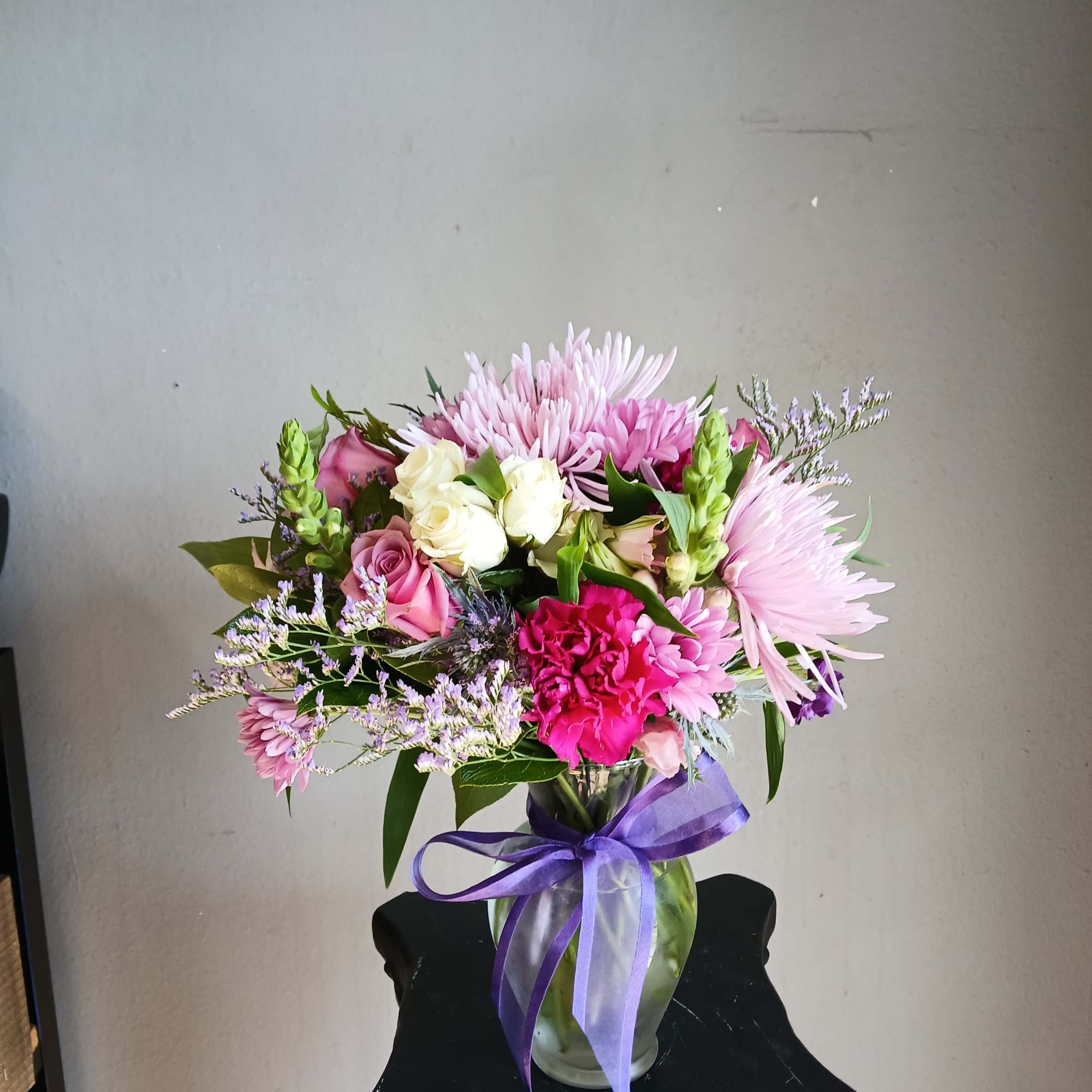 Pink and white mixed bouquet in a glass vase with a purple ribbon