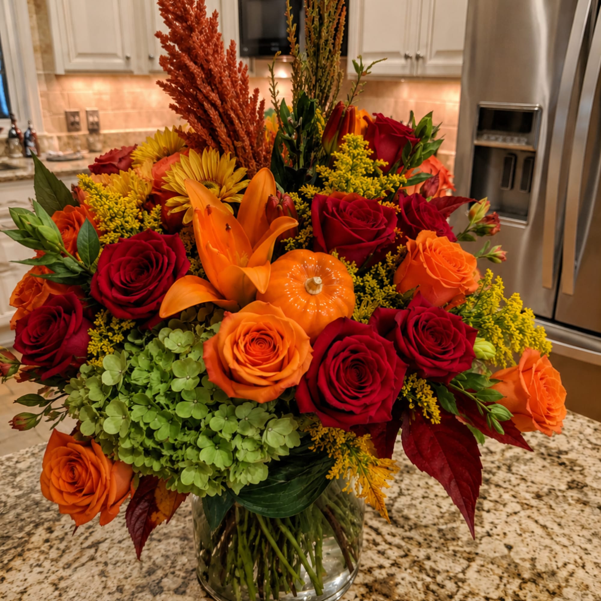 Autumn bouquet of red and orange roses with lilies in a glass vase