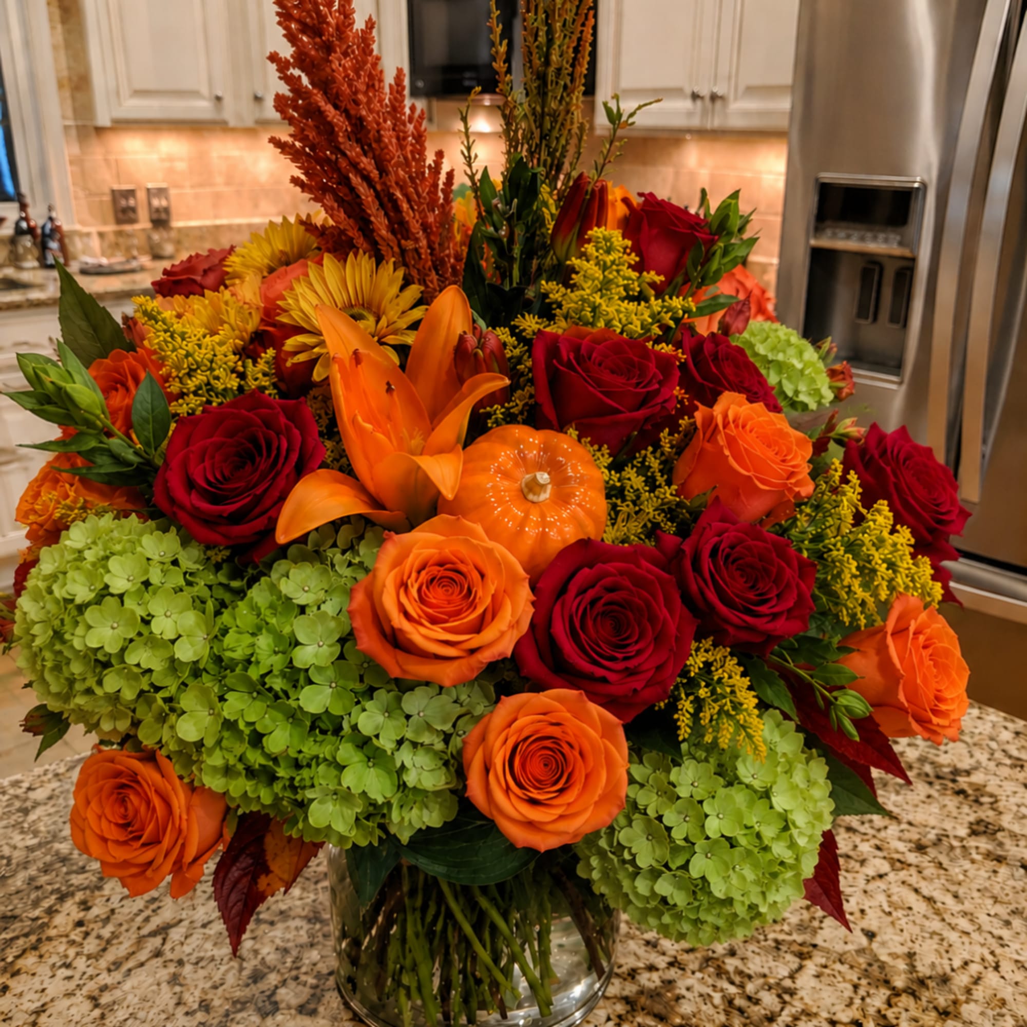 Orange and red roses with lilies and green hydrangeas in a glass vase