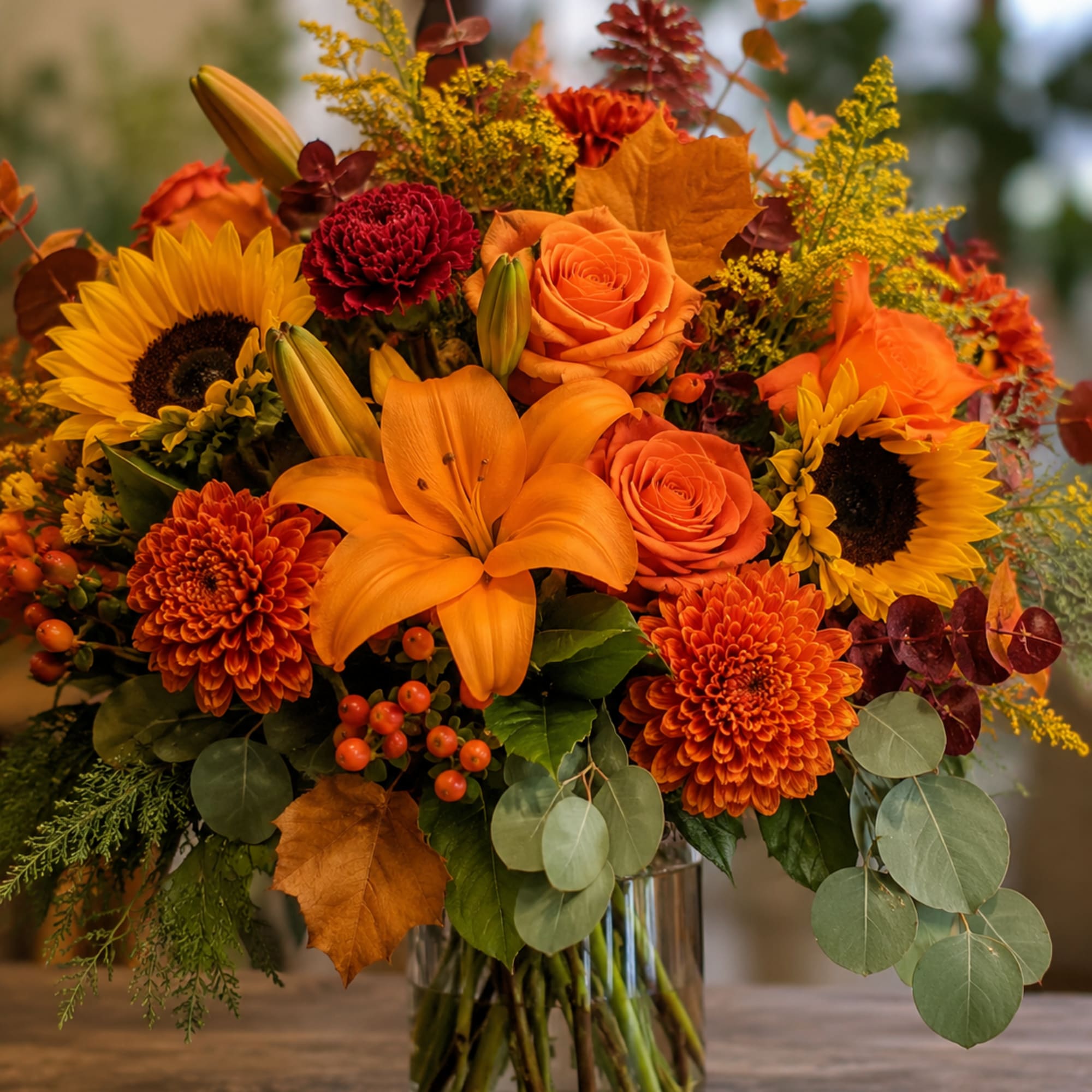 Autumn bouquet with orange lilies, roses, sunflowers, and chrysanthemums in a glass vase