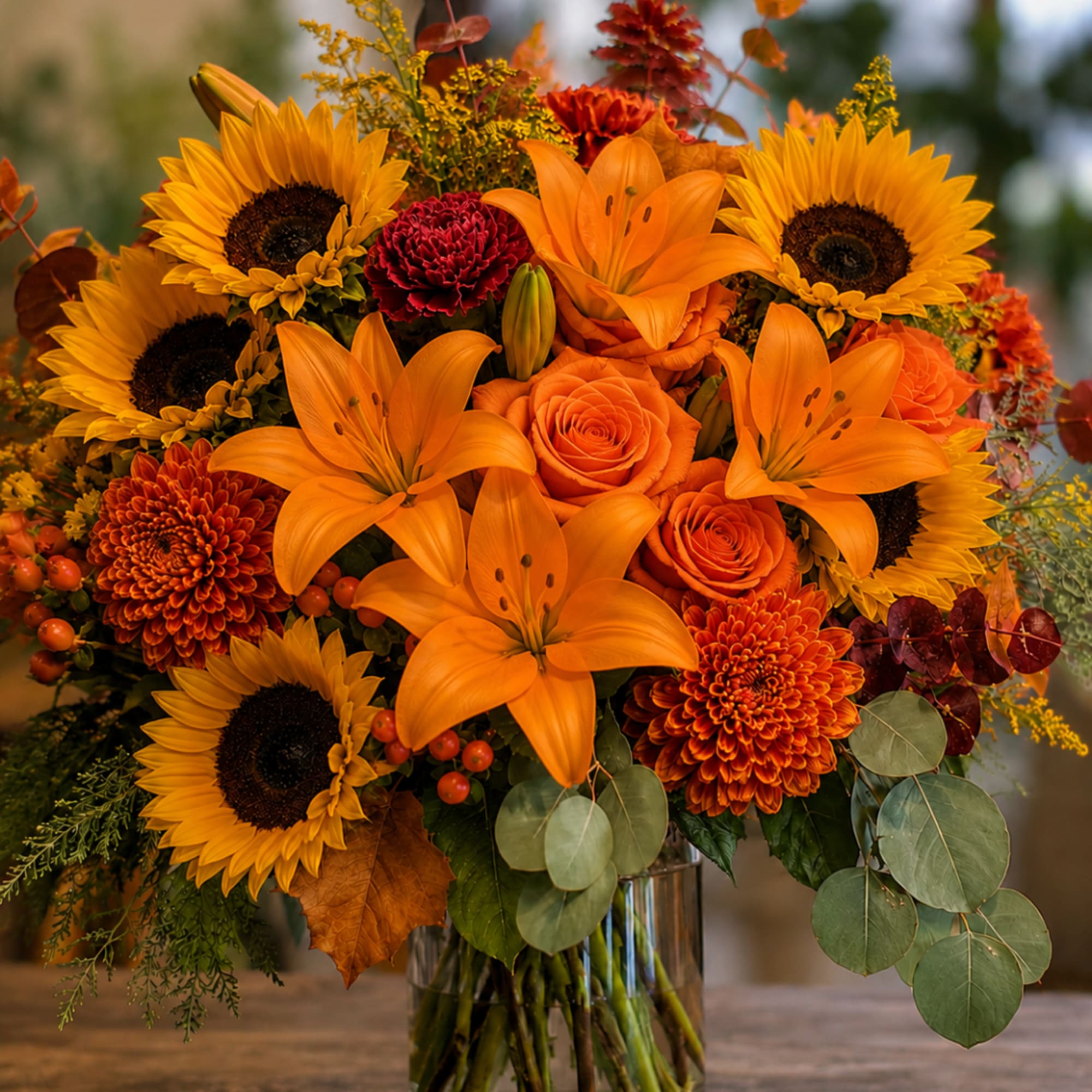 Orange lilies, sunflowers, and roses in a glass vase