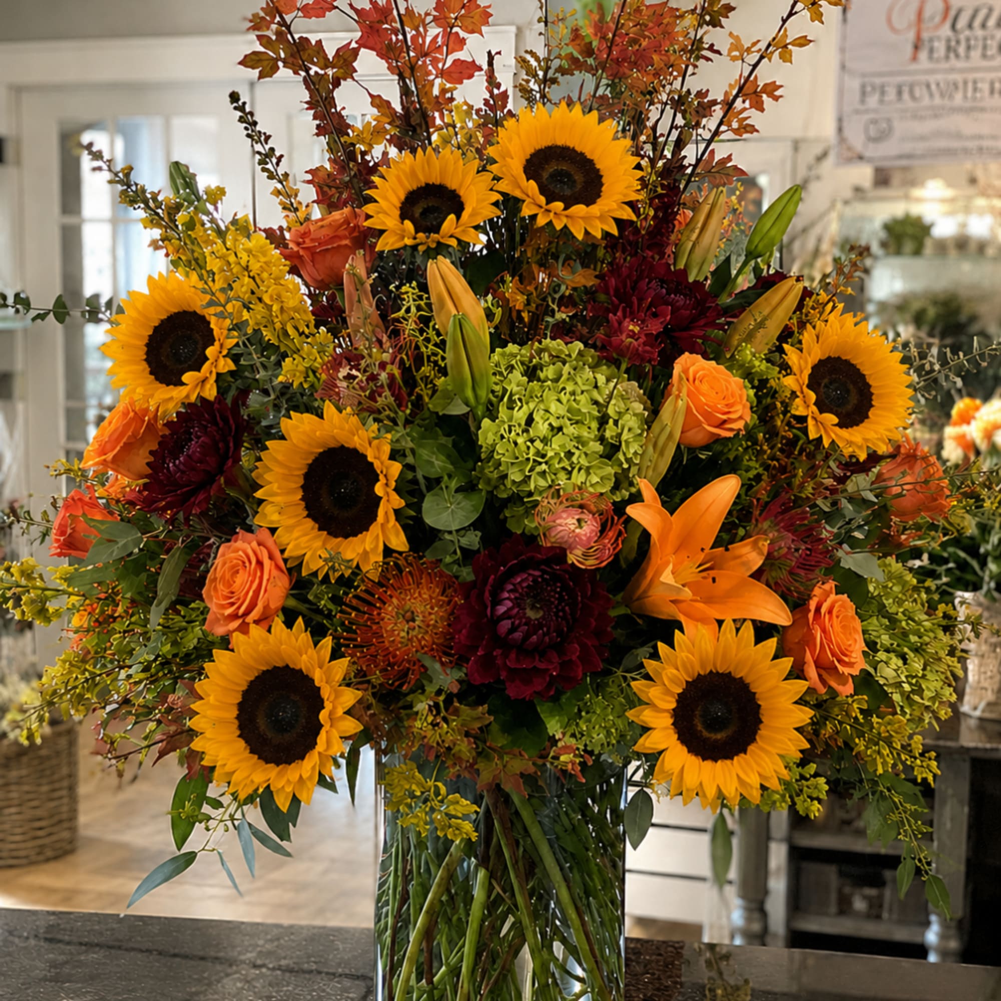 Large autumn bouquet with sunflowers, orange roses, and lilies in a glass vase