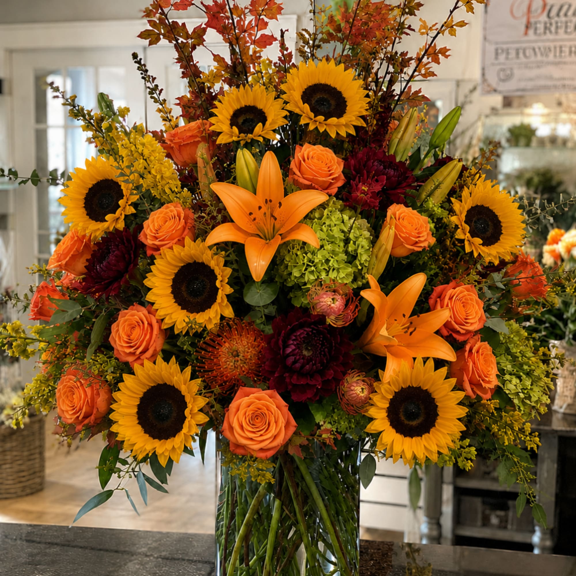 Large autumn bouquet with sunflowers, orange roses, and lilies in a glass vase