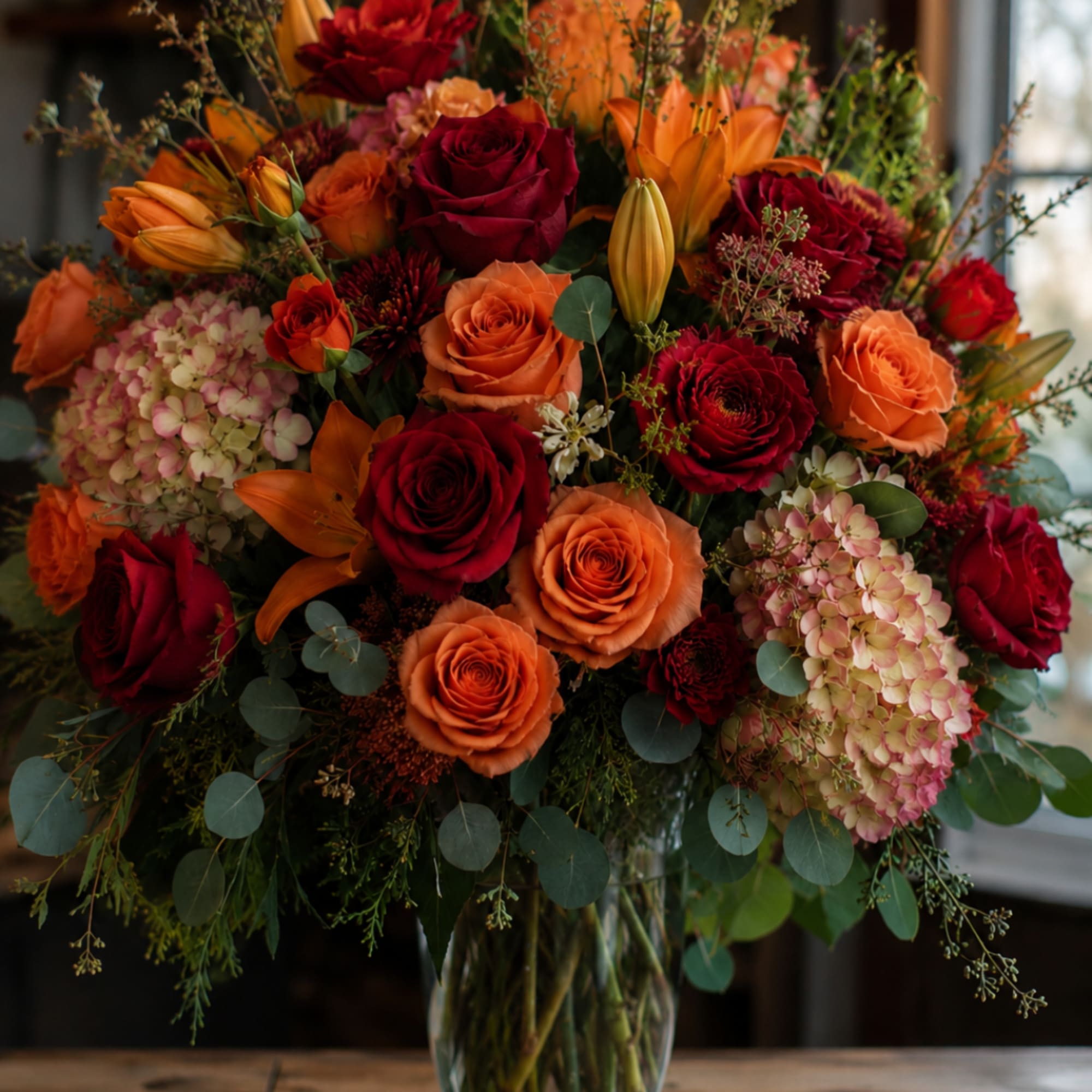 Bouquet of red and orange roses with lilies and hydrangeas in a glass vase
