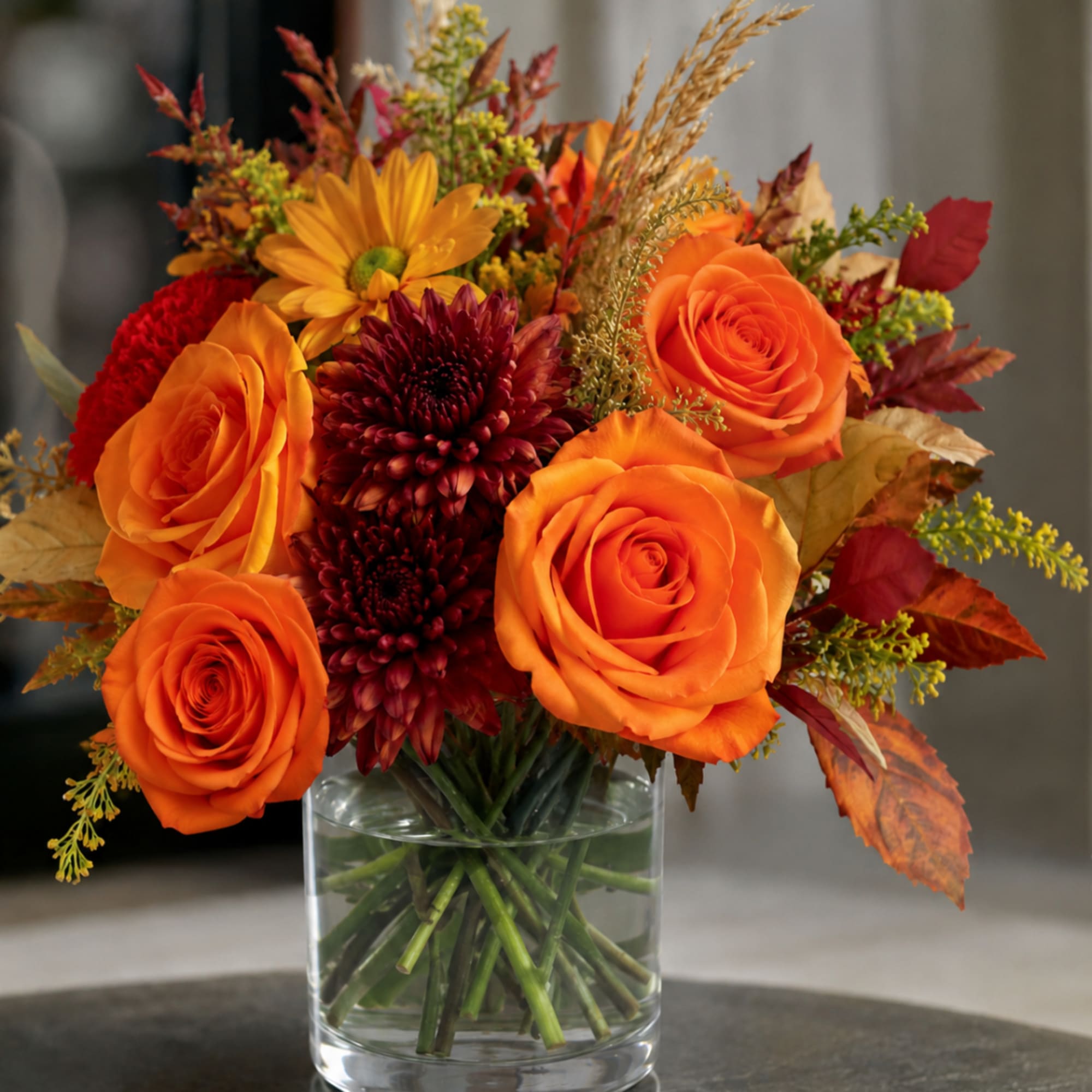 Orange roses and burgundy mums in a clear glass vase
