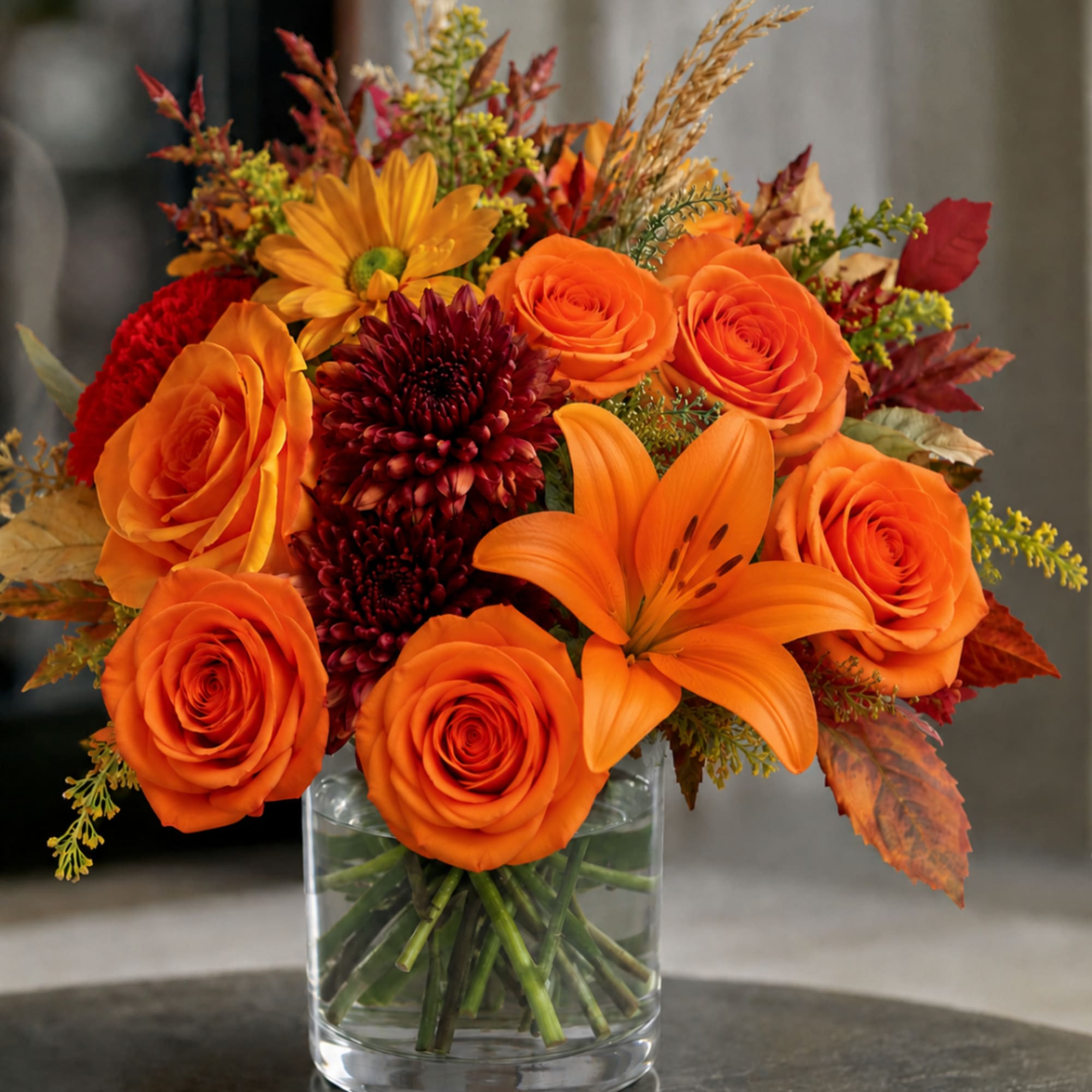 Orange roses and lilies in a clear glass vase with autumn accents