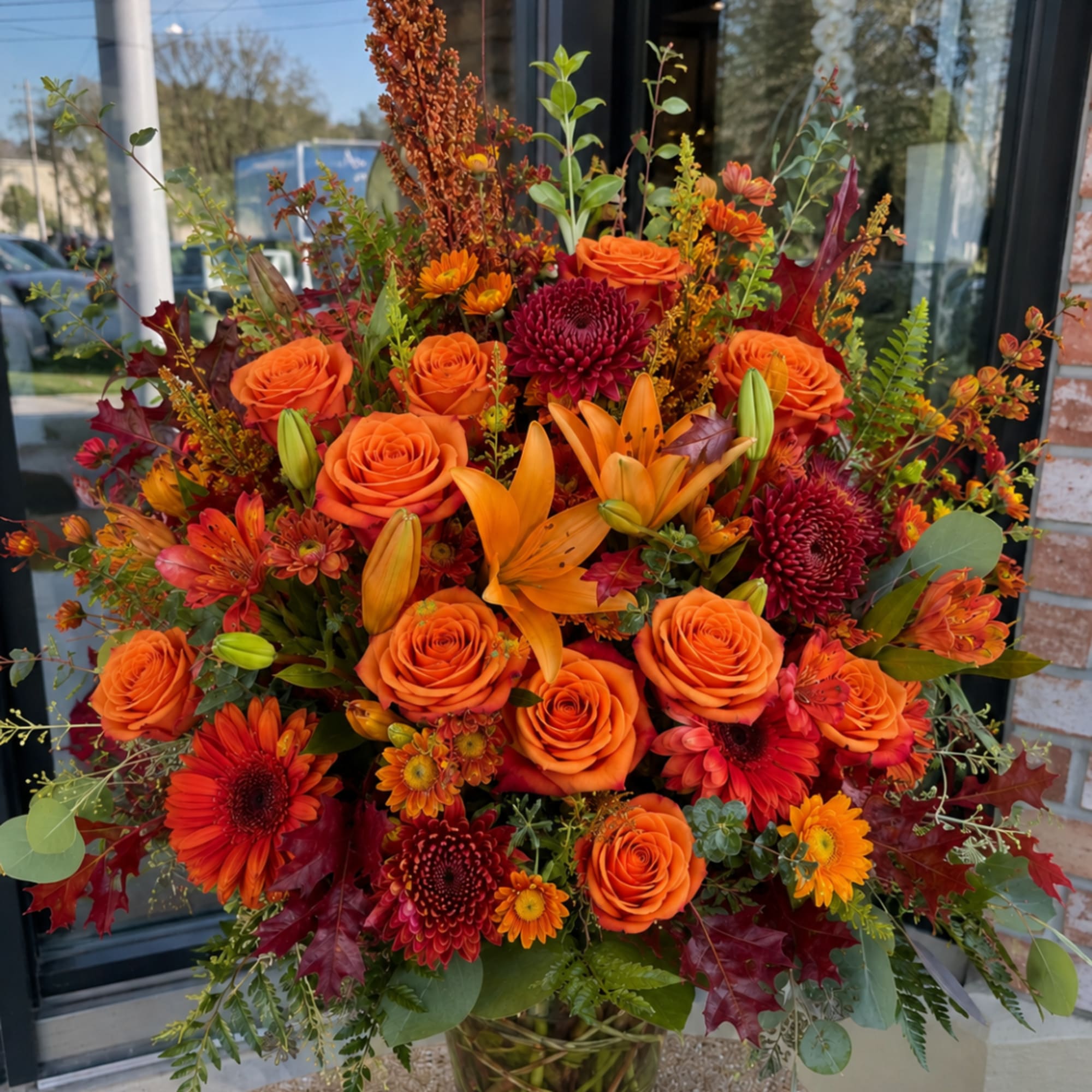Large bouquet of orange roses, lilies, and chrysanthemums in a glass vase