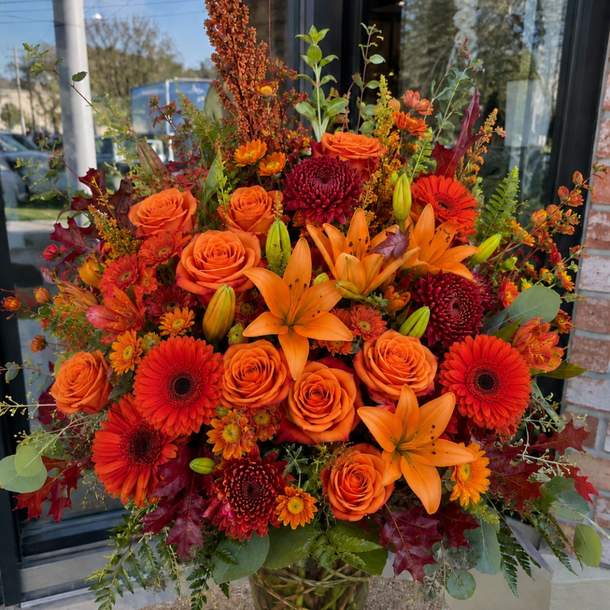 Orange roses, lilies, and gerbera daisies in a glass vase