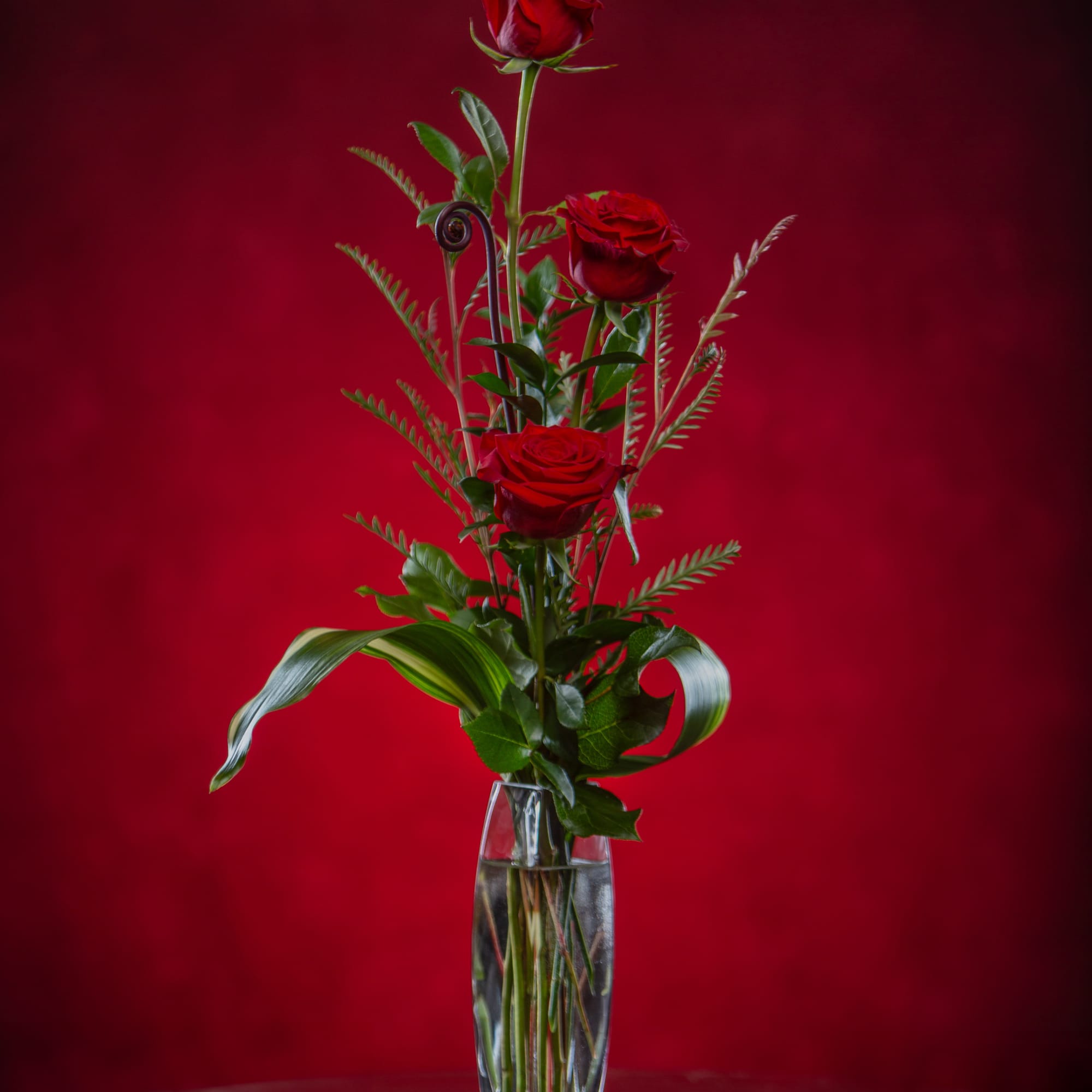 Three red roses in a clear glass vase against a red background