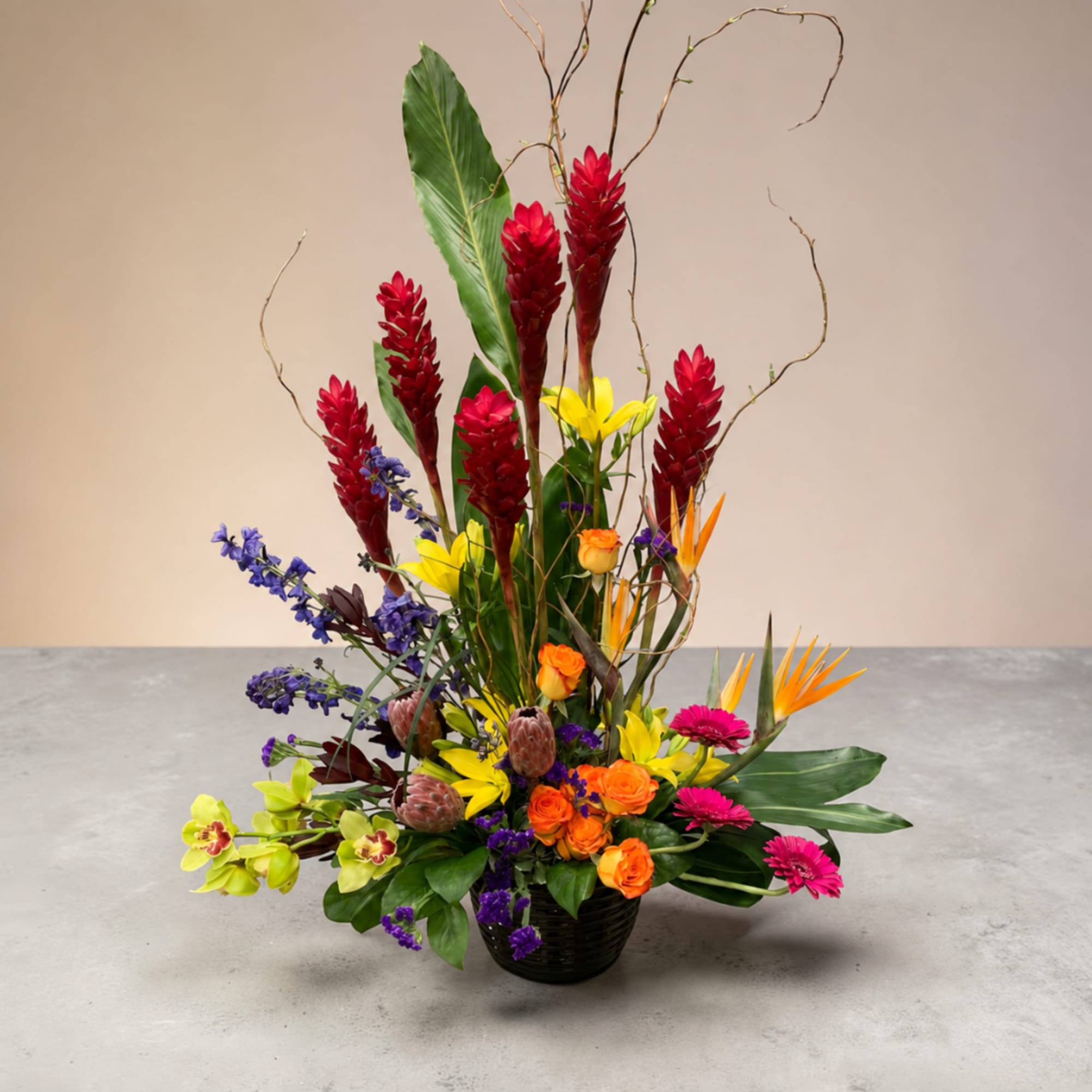 Tall tropical flower arrangement in a black basket with red, yellow, orange, and purple blooms