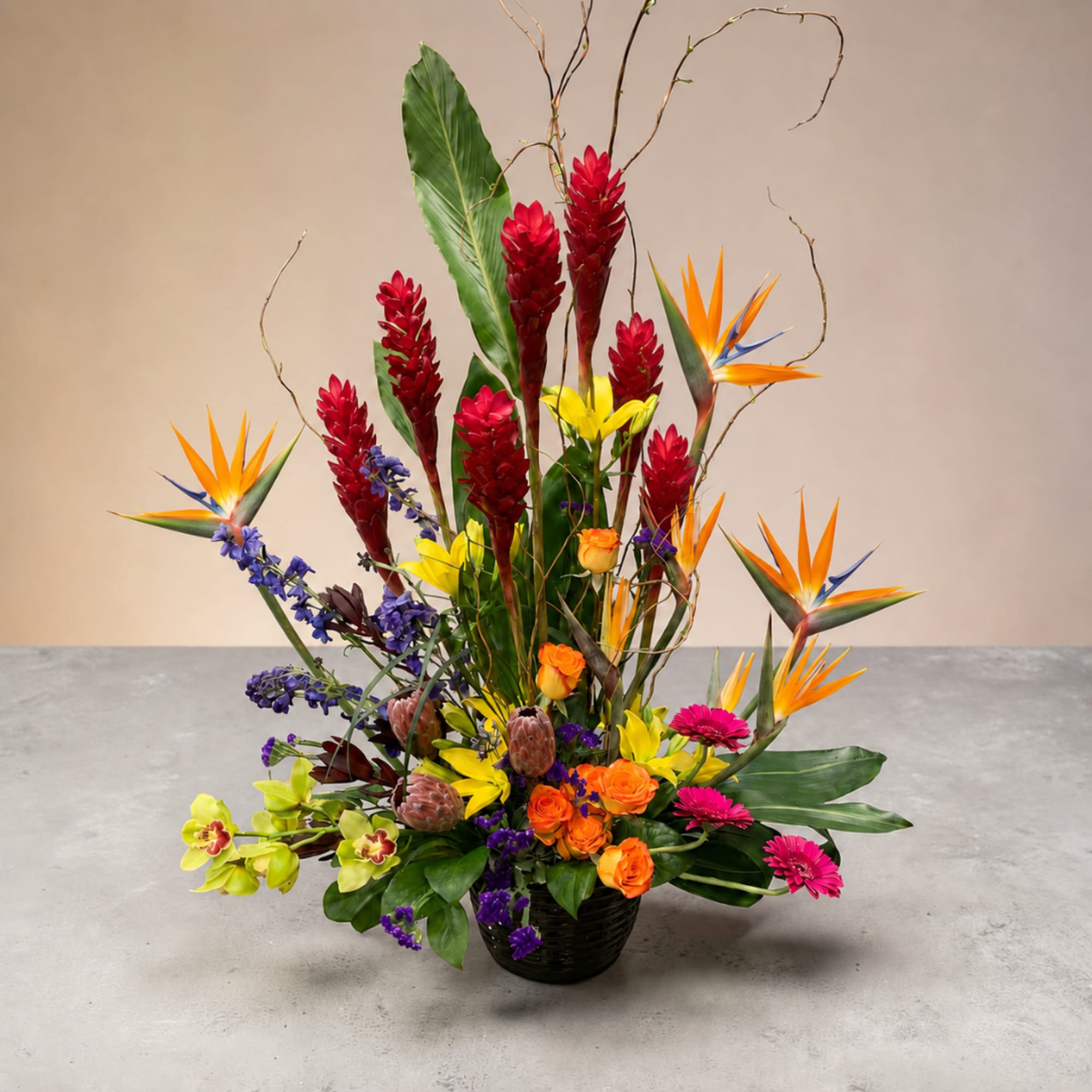 Tropical flower arrangement in a black basket with orange, red, yellow, and purple blooms