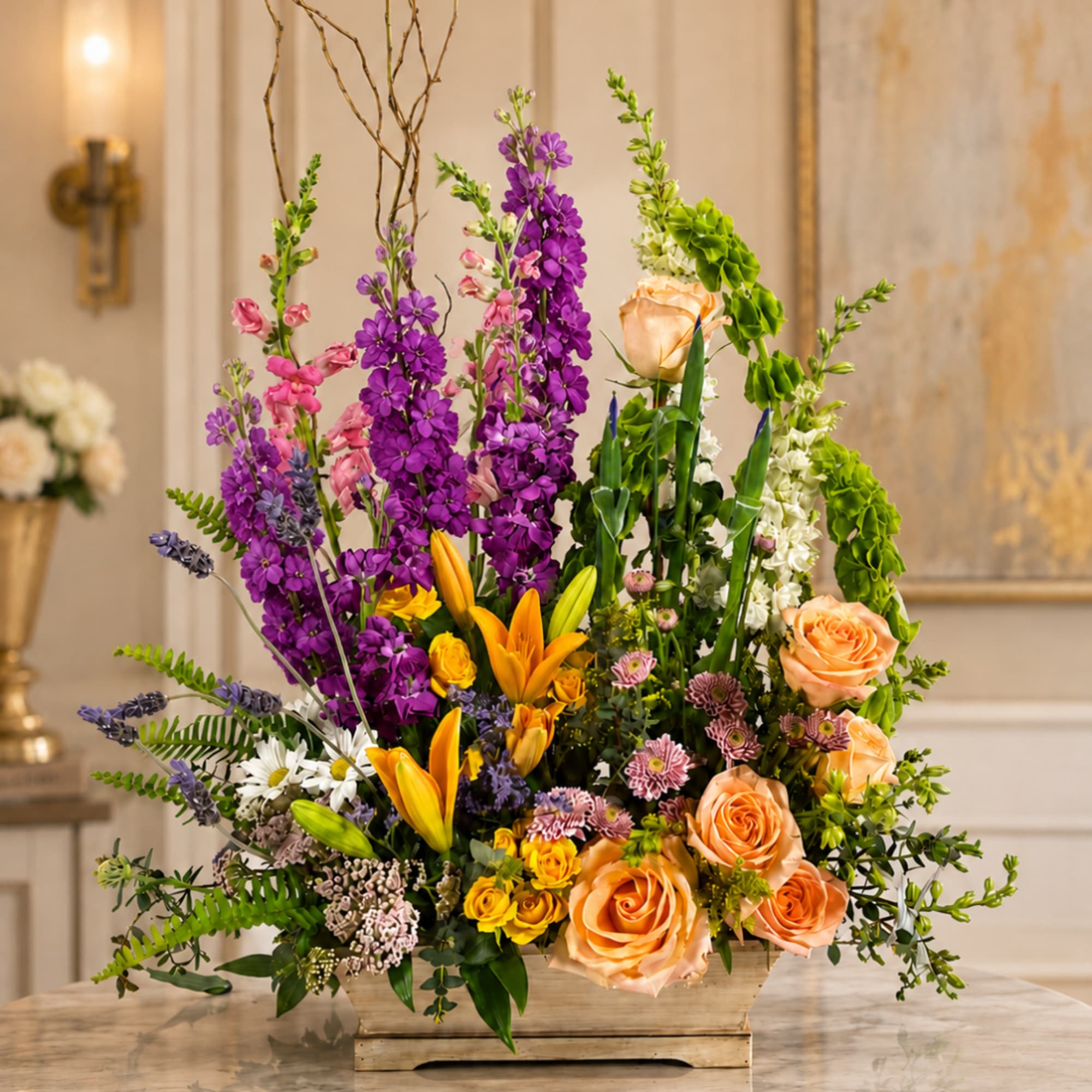 Tall mixed floral arrangement in a wooden container with purple, peach, and yellow blooms