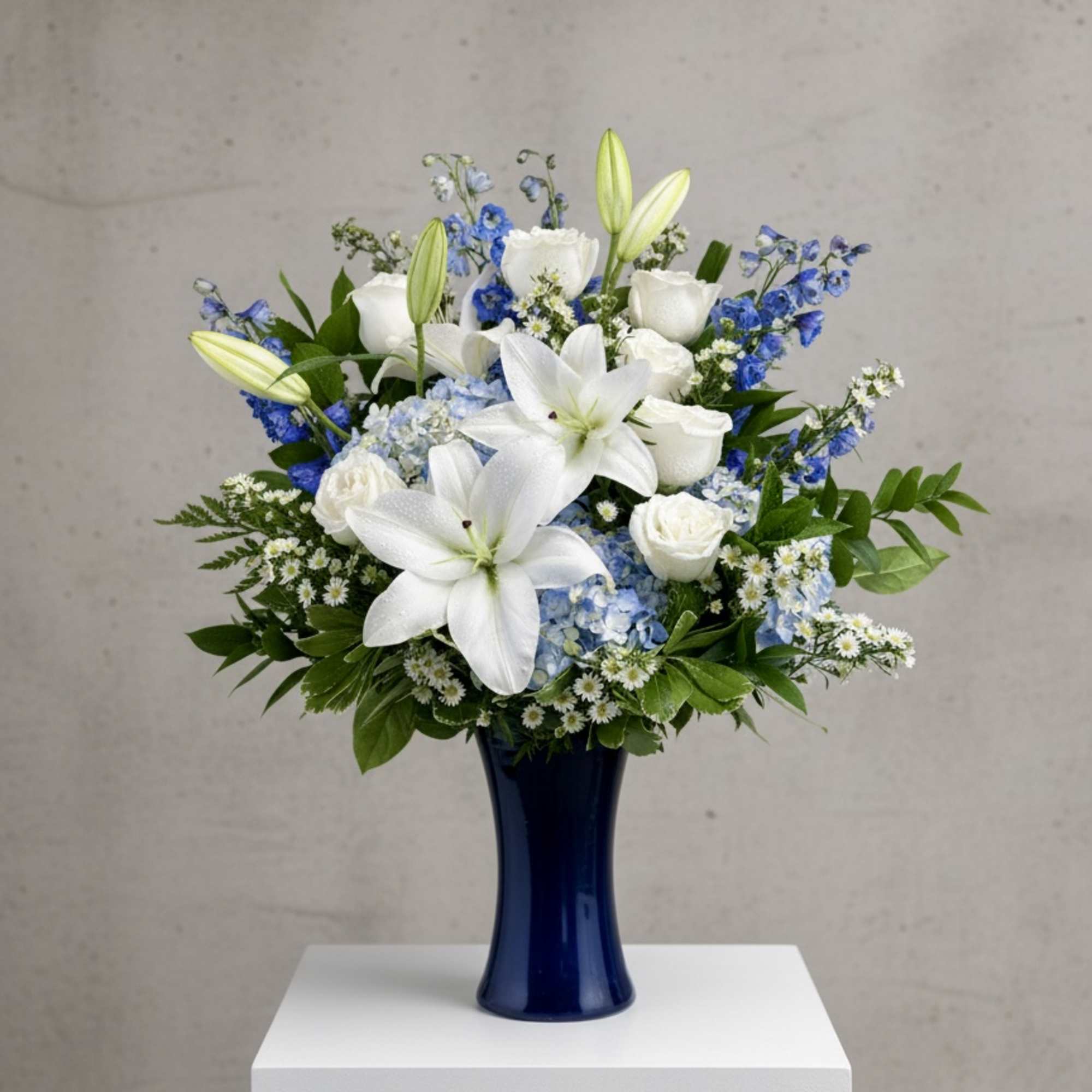 White lilies and roses arranged in a blue vase with blue accents