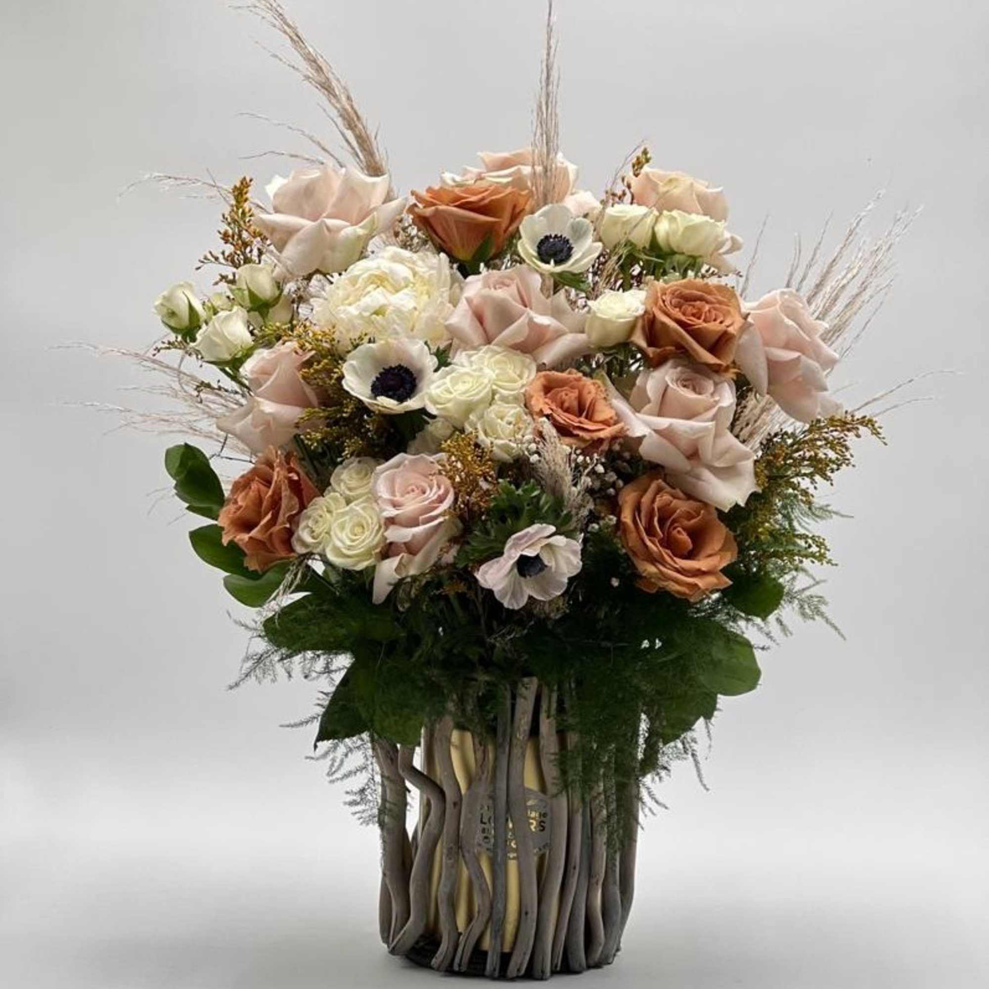 Bouquet of blush and peach roses with white accent flowers in a tall vase