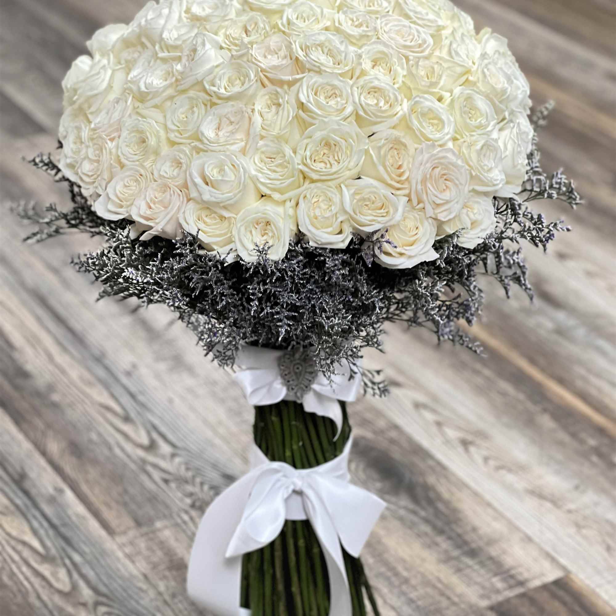 Large bouquet of white roses with dark filler and a white ribbon wrap