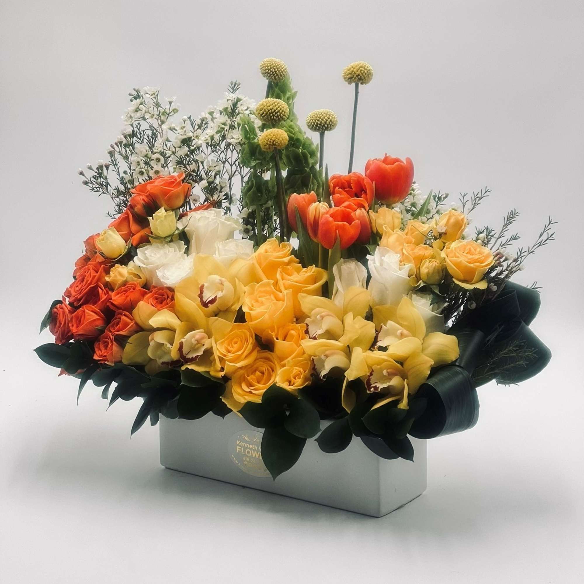 Mixed bouquet of orange, yellow, and white flowers in a rectangular box