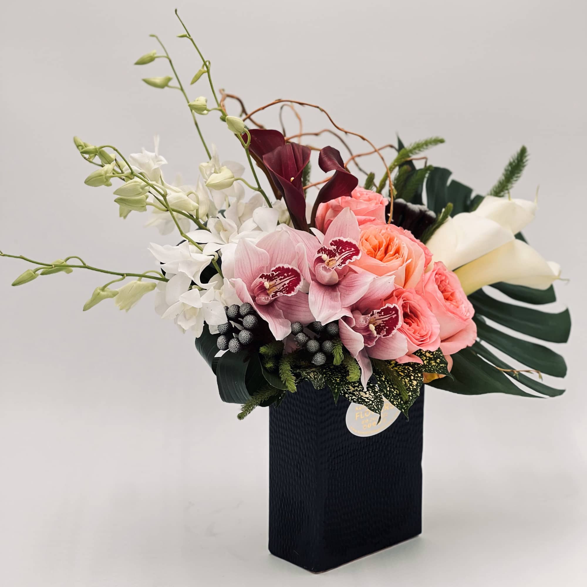 Mixed bouquet with pink roses, orchids, and white calla lilies in a black vase