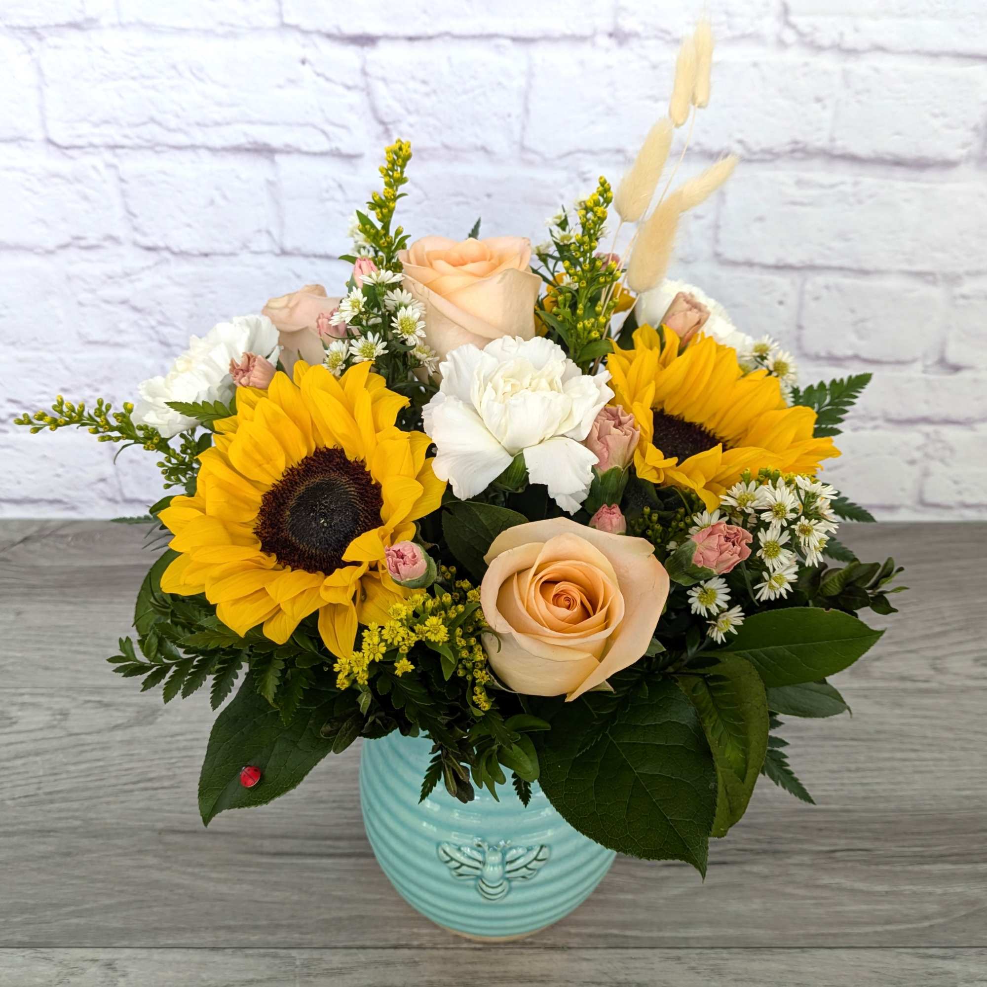 Mixed bouquet with sunflowers, roses, and white blooms in a blue vase