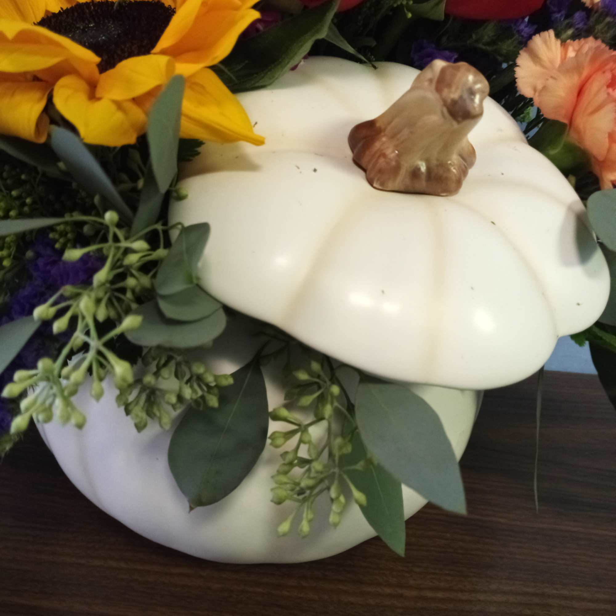 Mixed floral arrangement in a white pumpkin container with a sunflower and red blooms