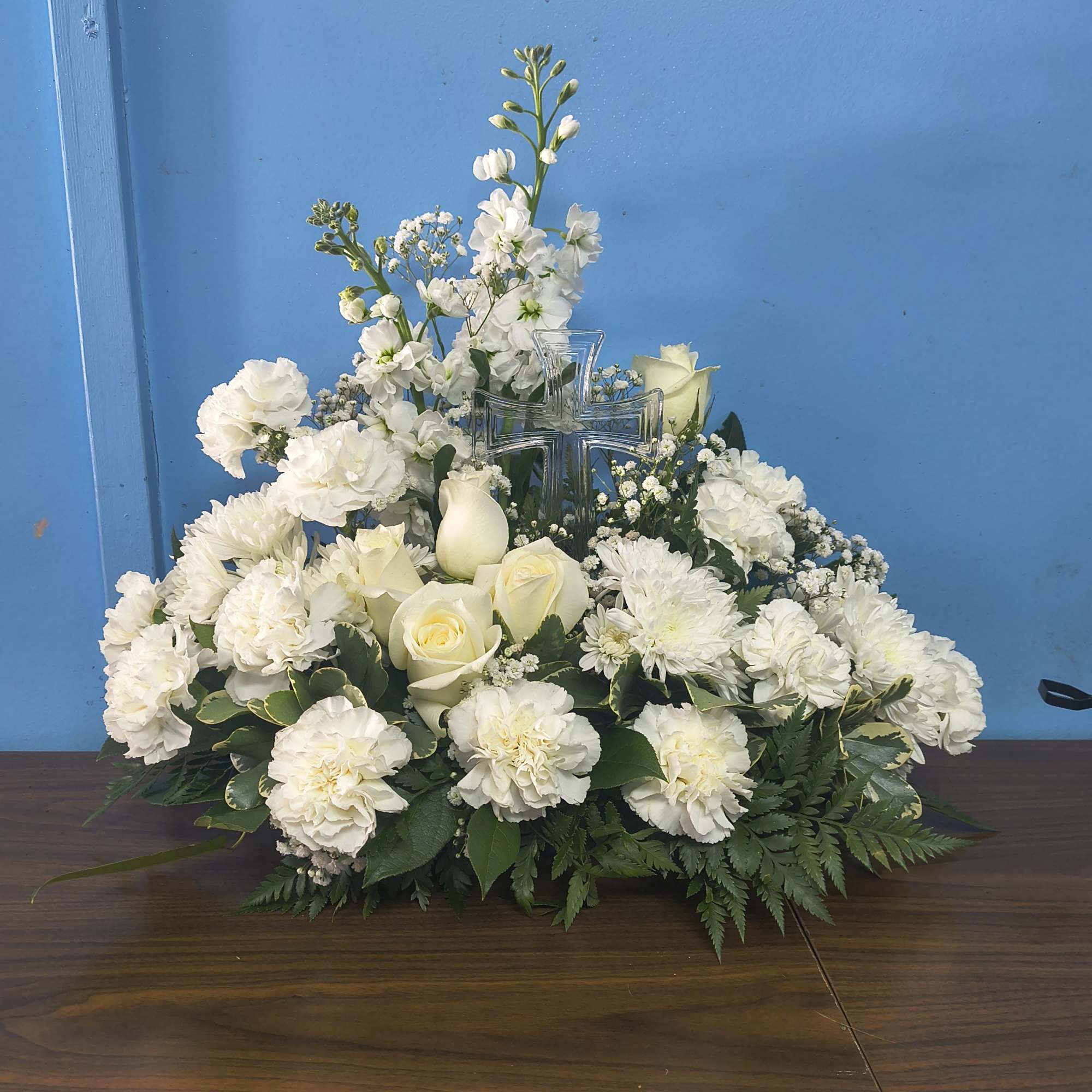 A low, oval spray of creamy white roses, ruffled carnations, and cushion