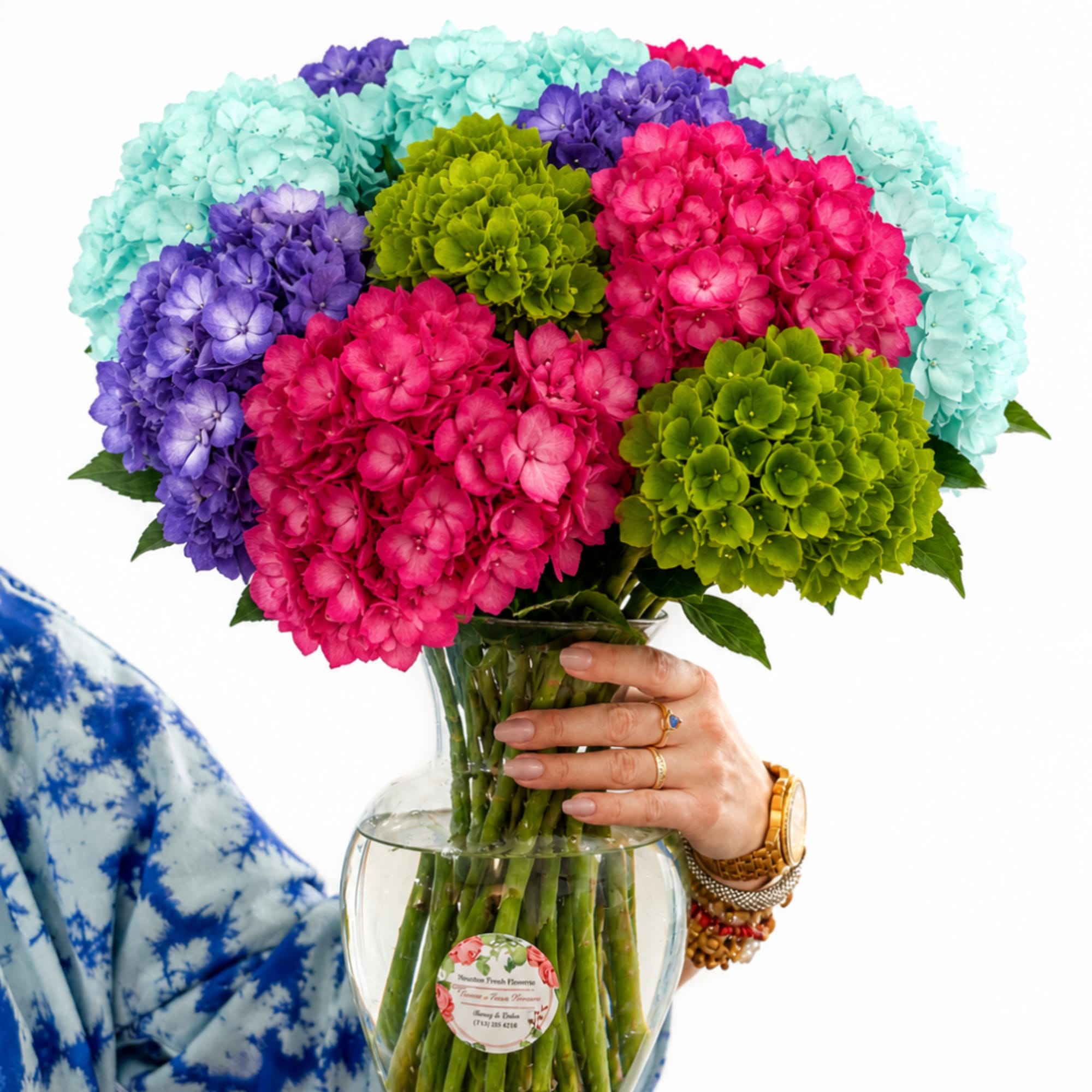 Colorful hydrangea bouquet in a clear glass vase being held by a hand