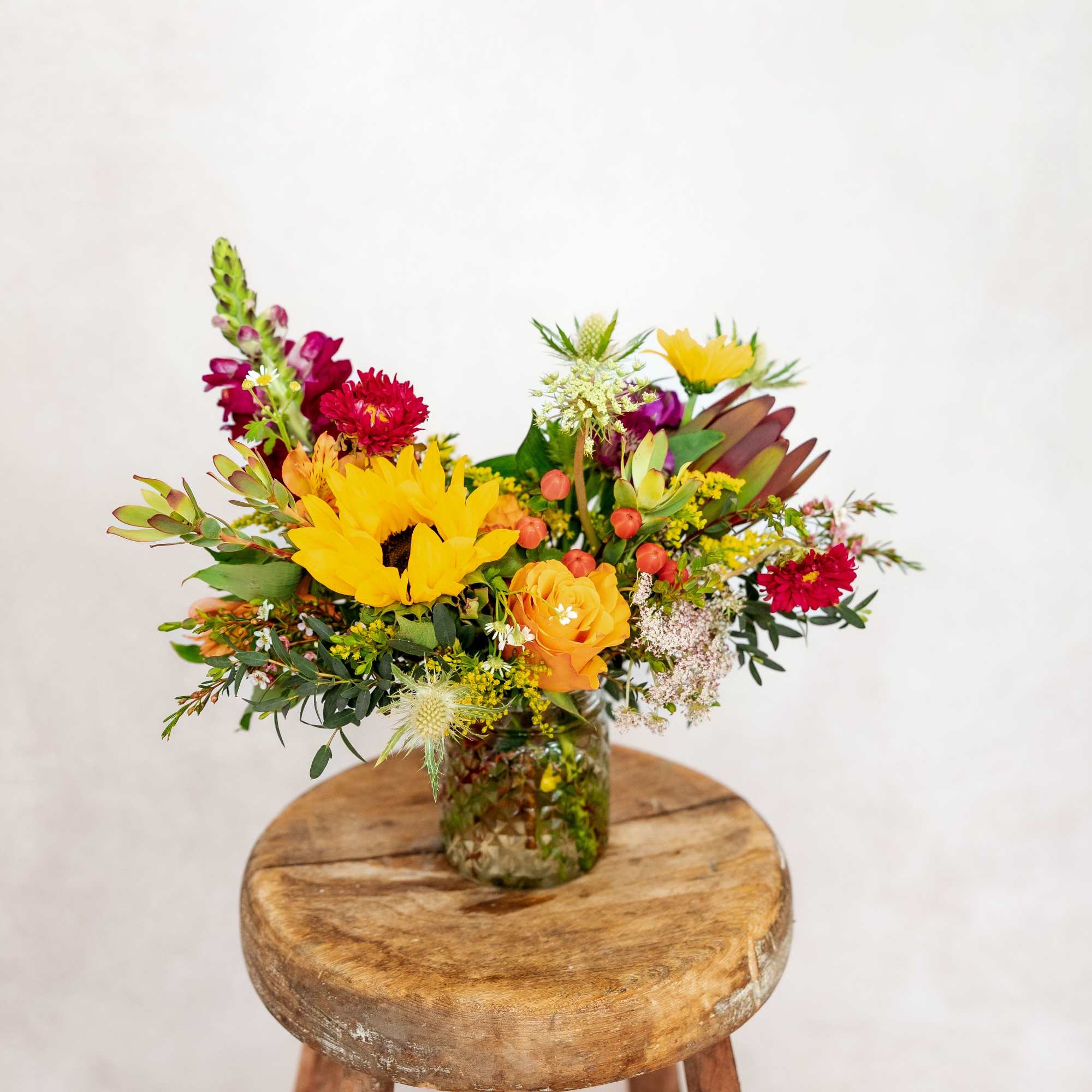 Mixed bouquet with sunflowers, roses, and red blooms in a glass jar