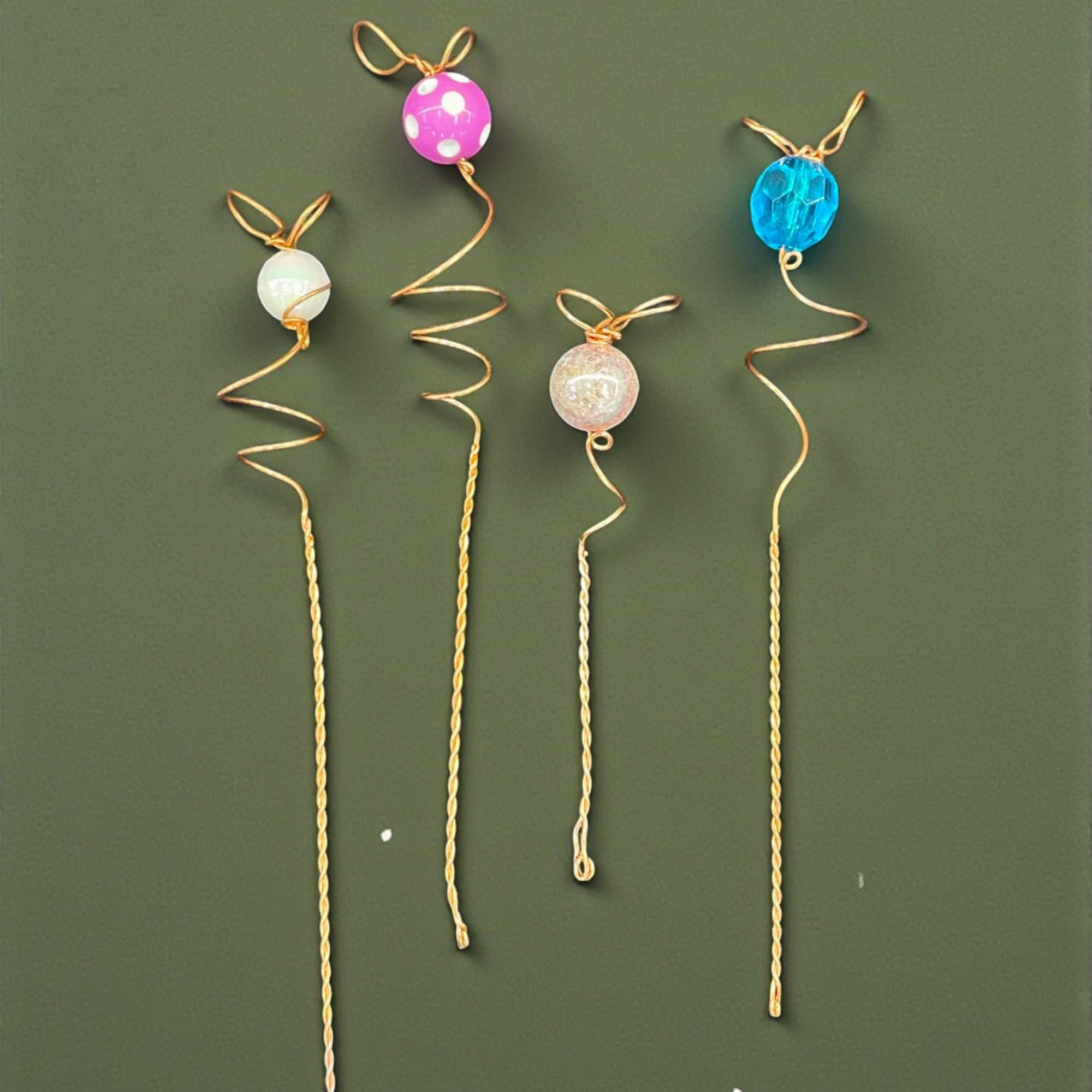 Four decorative wire picks with colorful bead tops on a green background