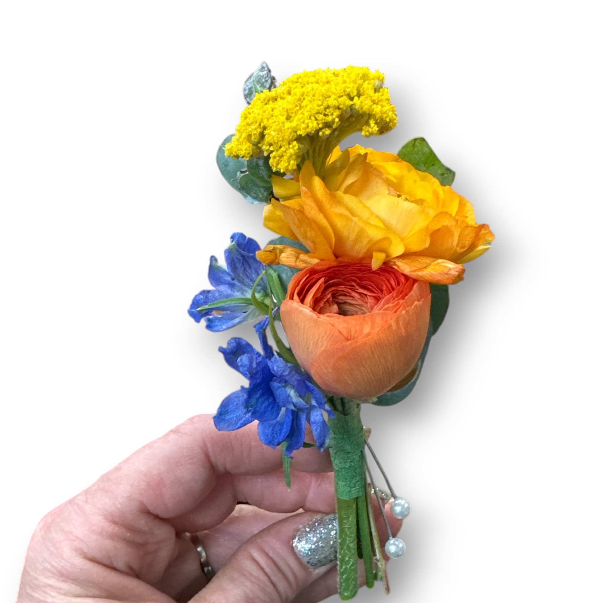 Small boutonniere with orange and yellow blooms and blue flowers held in a hand.