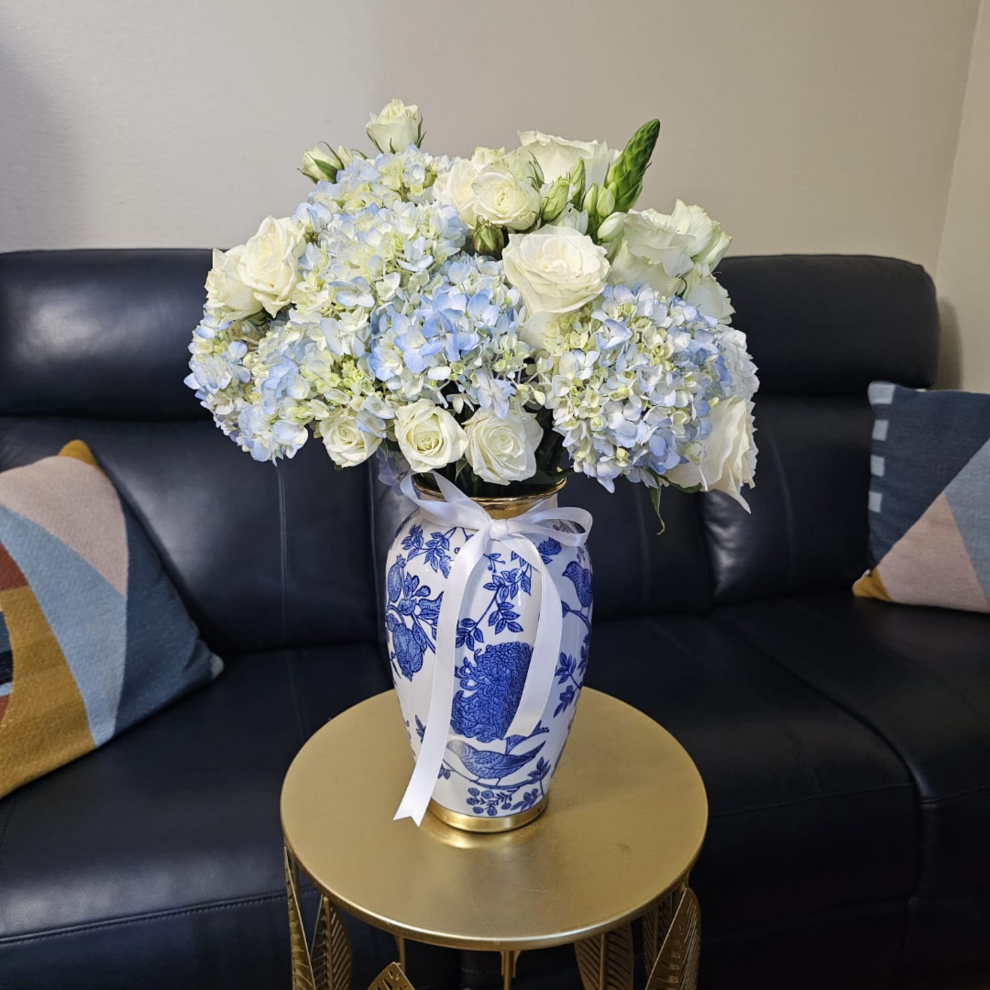 White roses and blue hydrangeas in a blue-and-white vase with a ribbon