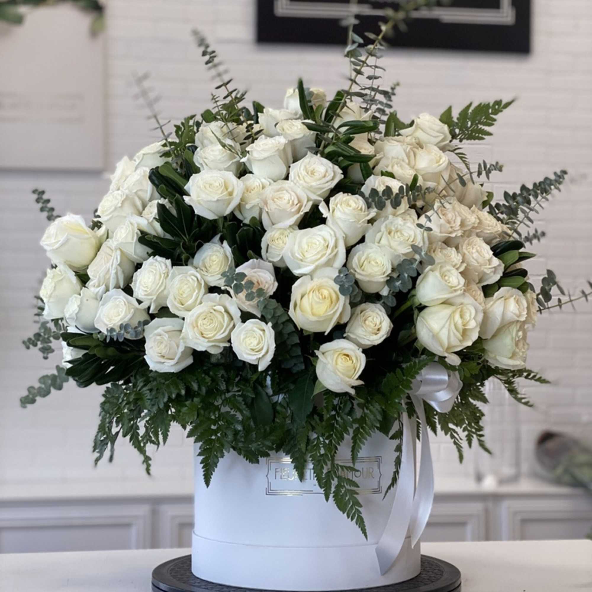 Large white rose arrangement in a round white box with greenery