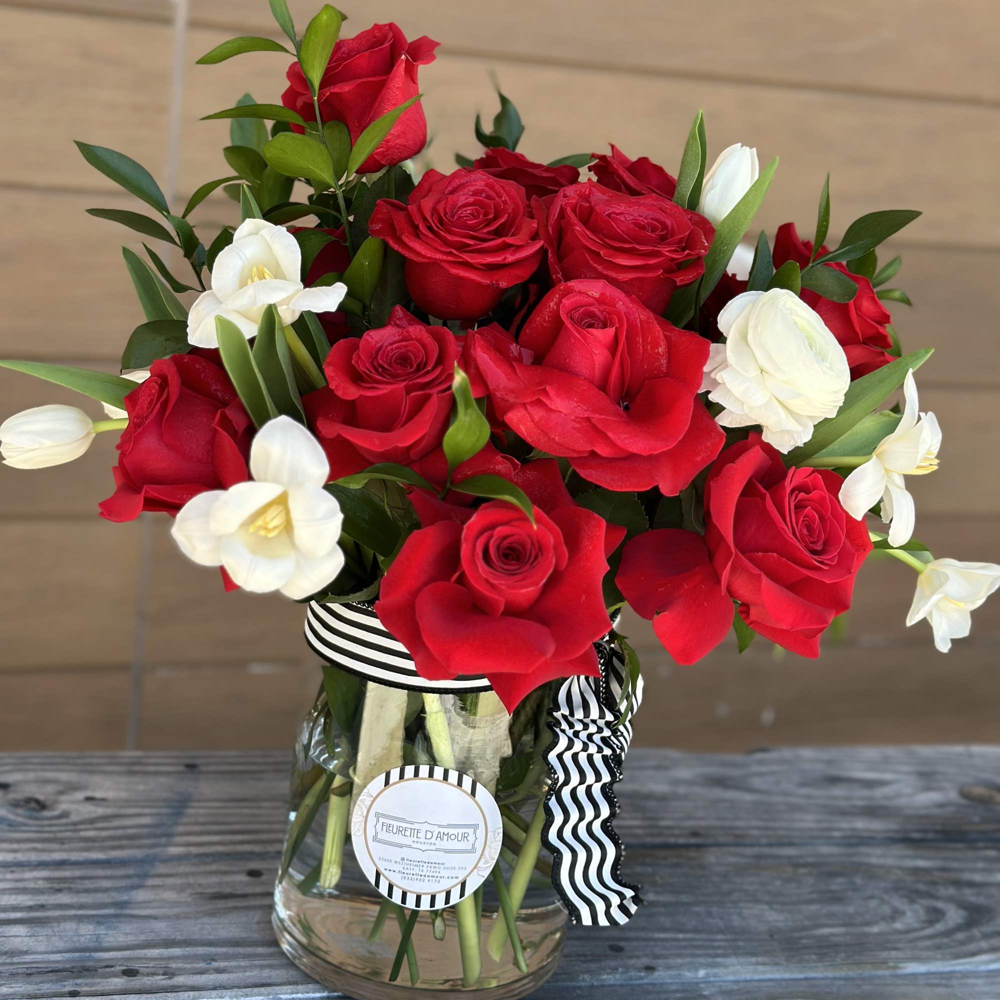 Red roses and white flowers arranged in a glass vase with a striped ribbon.