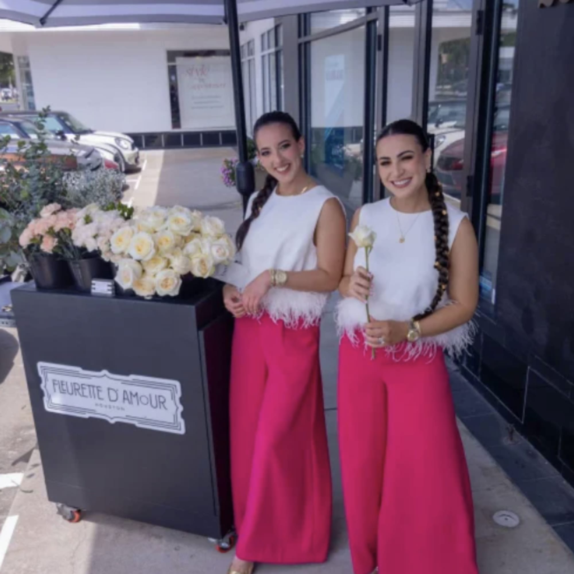Two women stand beside a cart of white and pink roses.