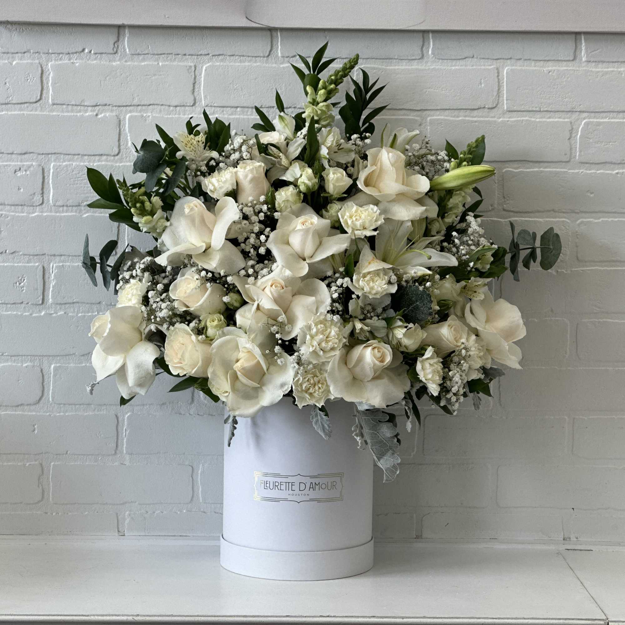 White floral arrangement in a round hatbox with greenery