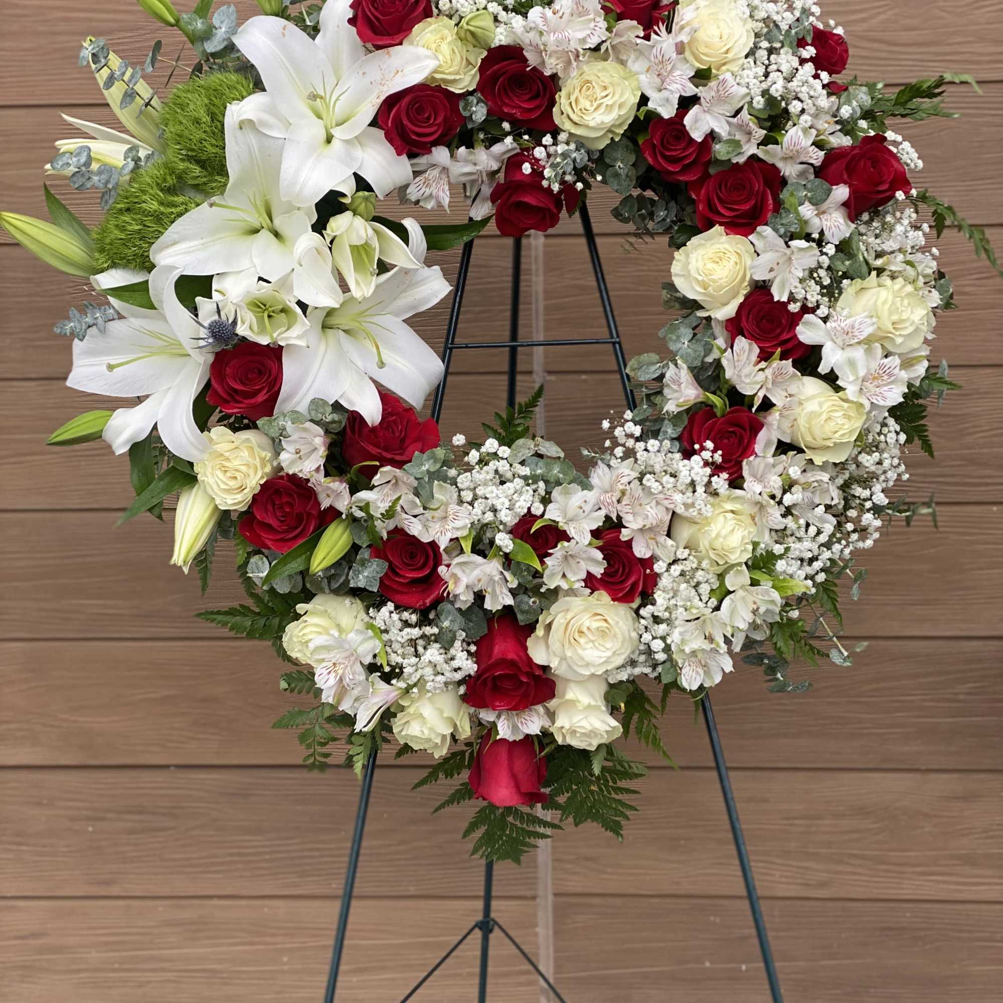 Heart-shaped floral wreath with red and white roses and lilies on a stand