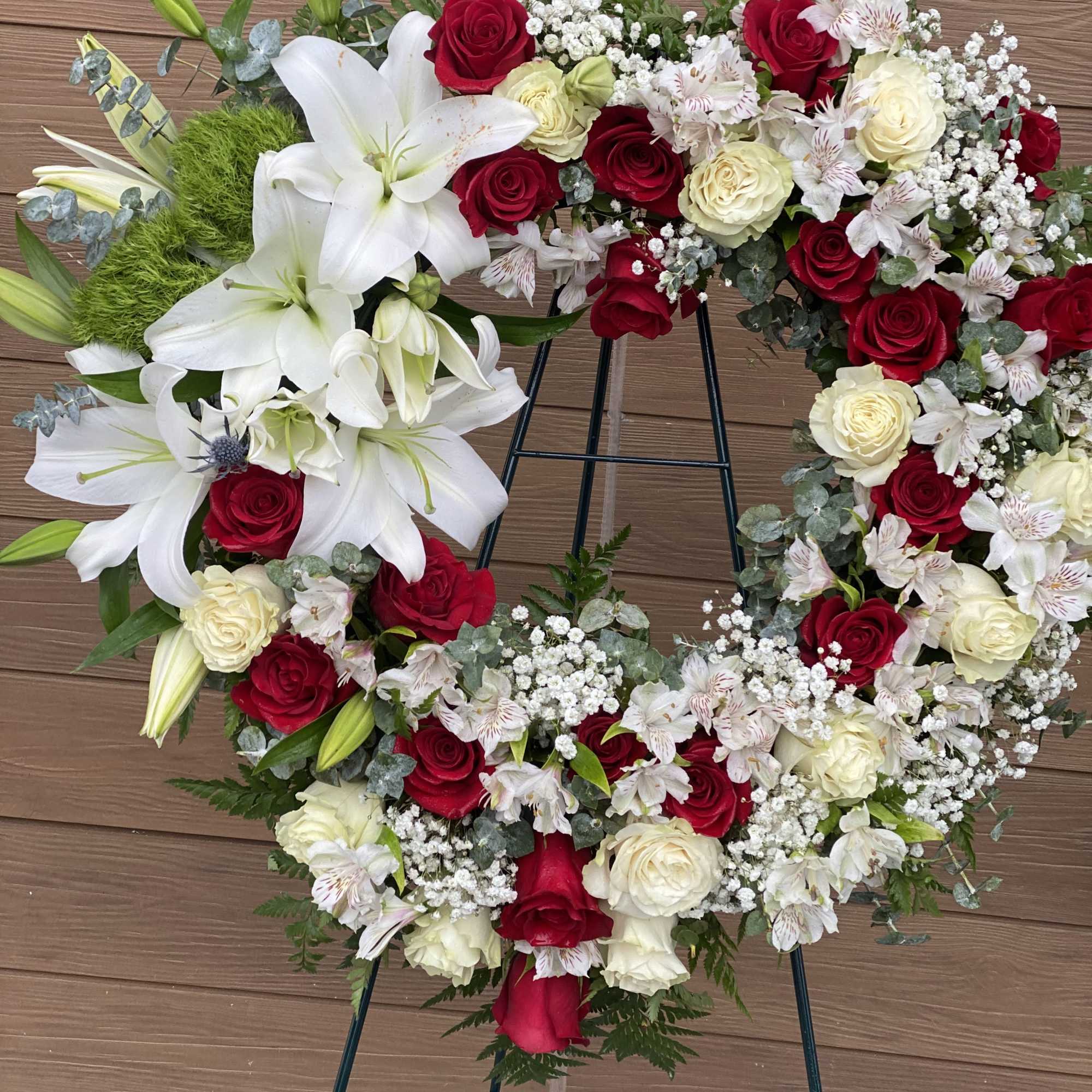 Heart-shaped wreath of red and white roses with lilies on a stand