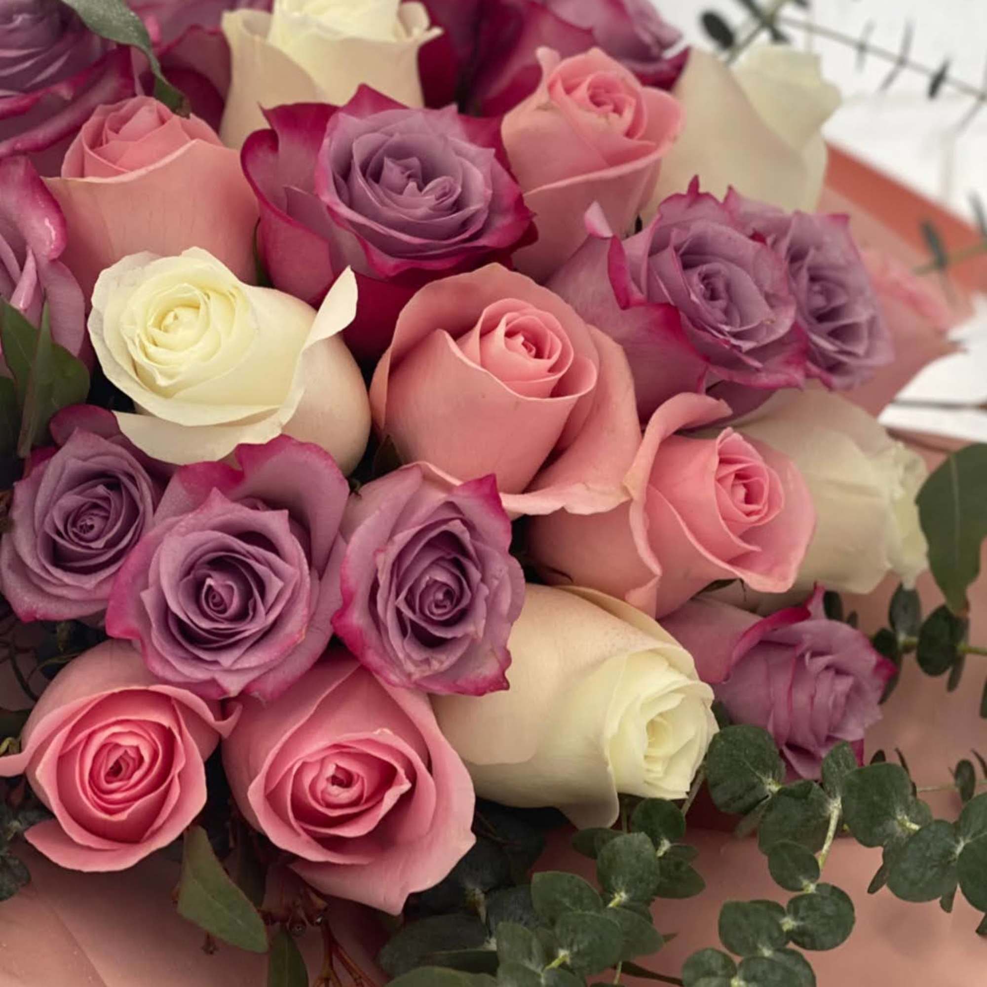 Bouquet of pink, purple, and white roses wrapped in blush paper