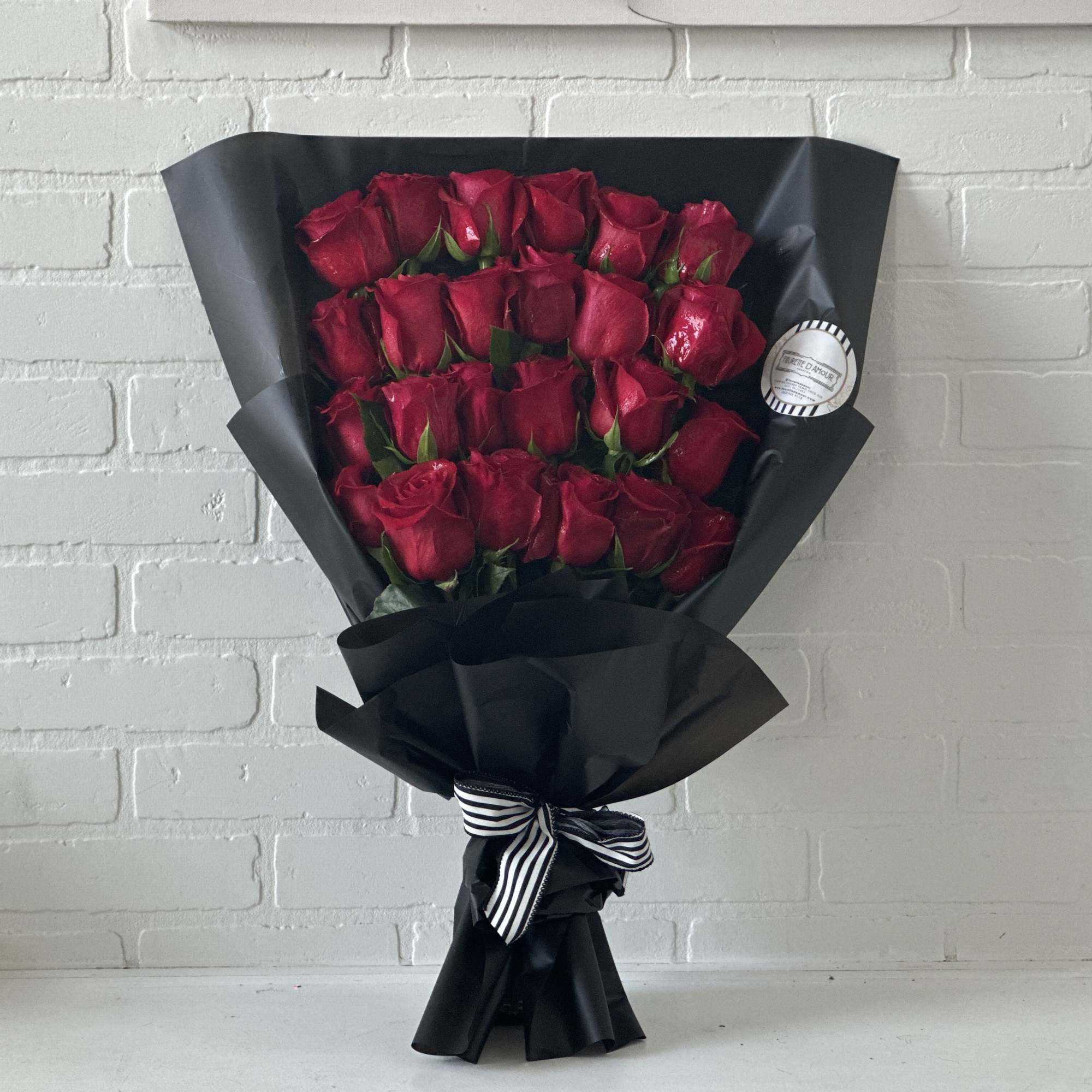 Bouquet of red roses wrapped in black paper with a striped ribbon
