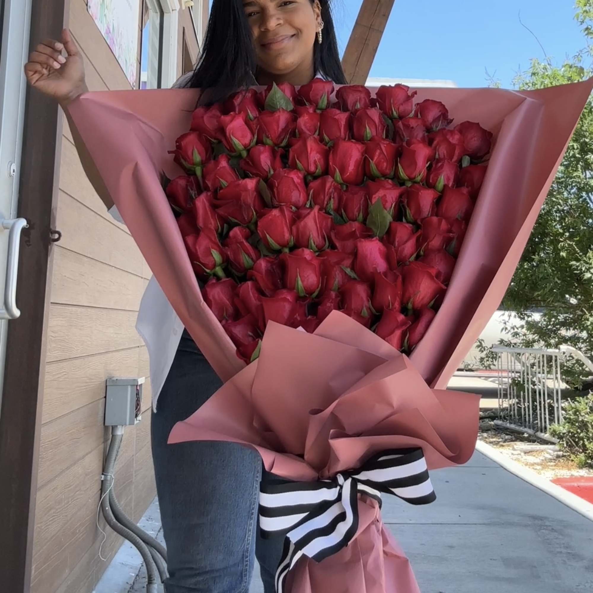 Woman holding a large bouquet of red roses wrapped in pink paper