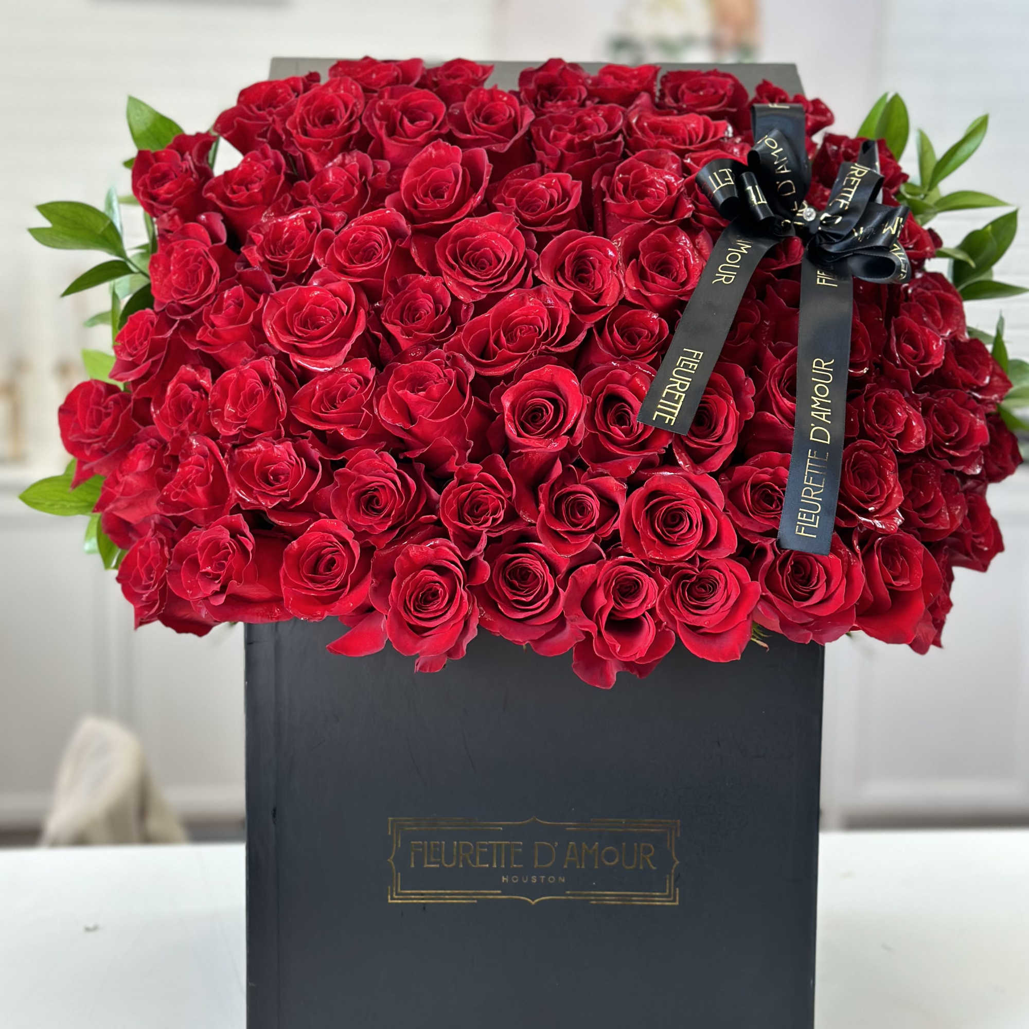 Large box of red roses with a black ribbon bow